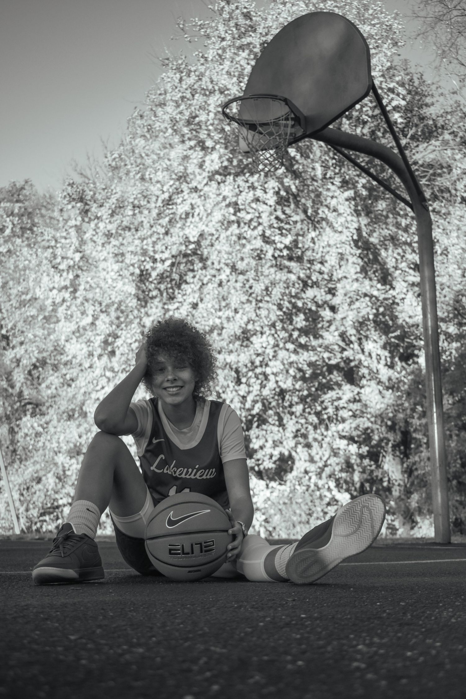 Black and white photo of basketball practice on an outdoor court with trees in background.