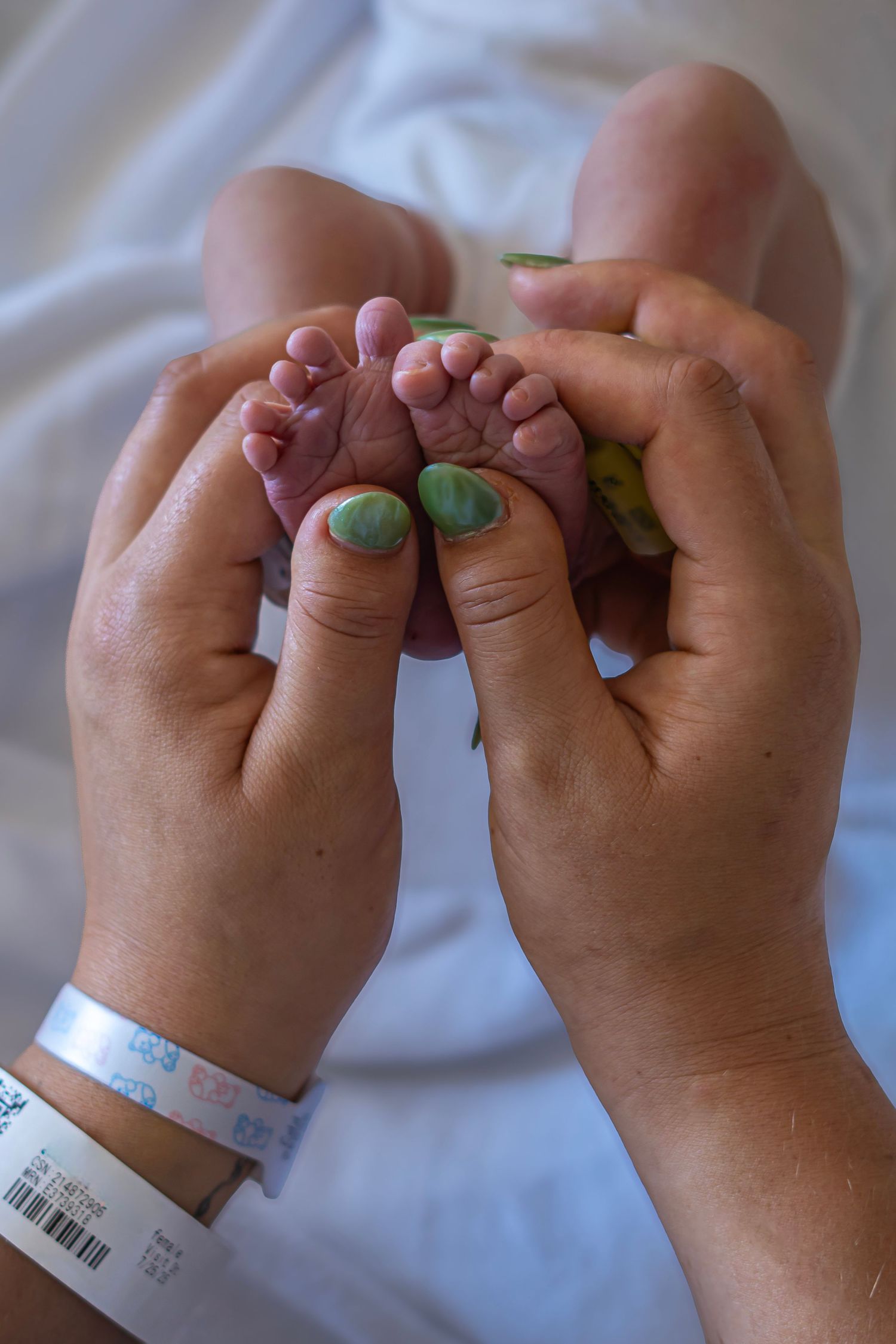 Close up of hands wearing hospital bracelets intertwined with painted fingernails.
