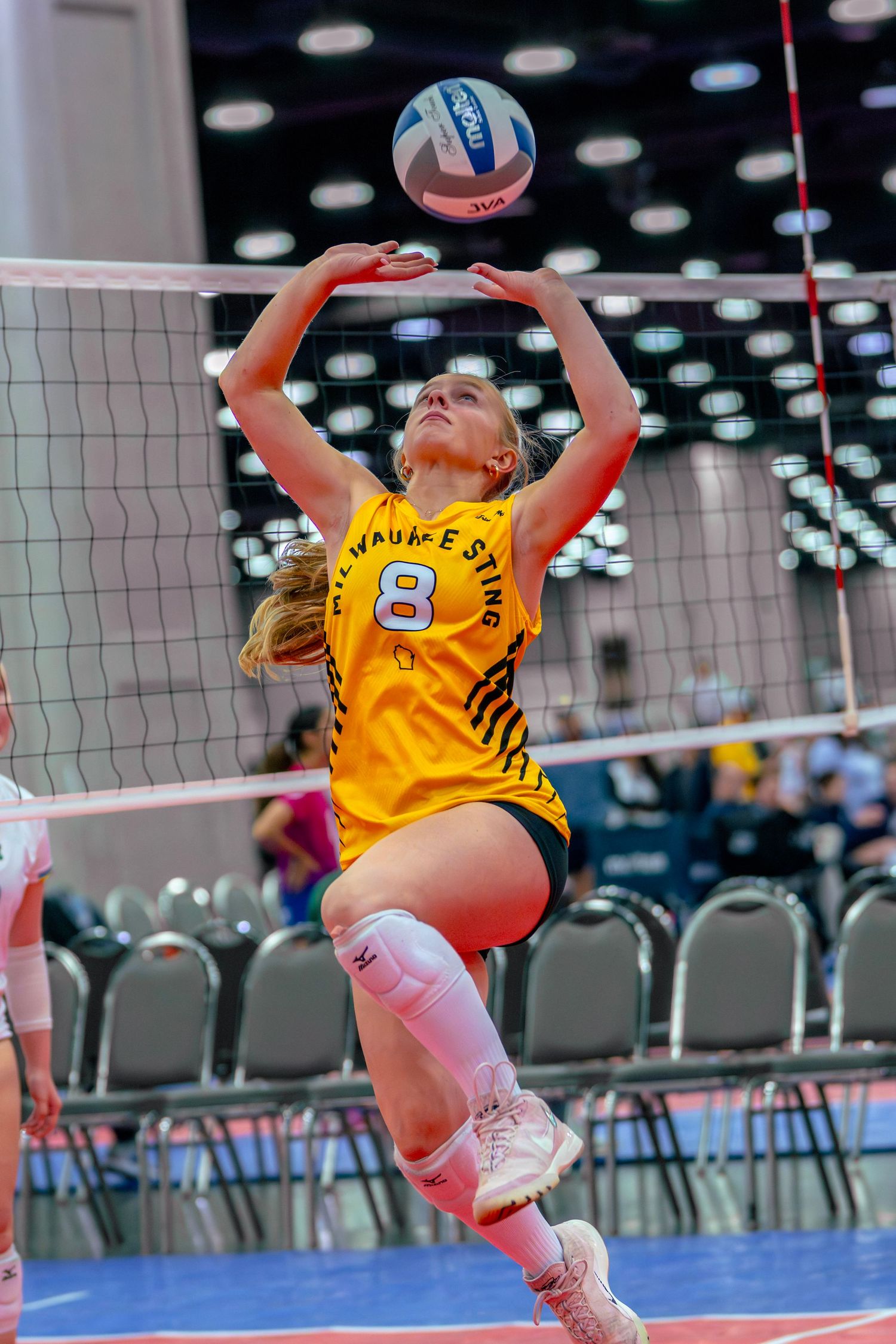 Female volleyball player in yellow jersey number 8 setting the ball during an indoor tournament match.