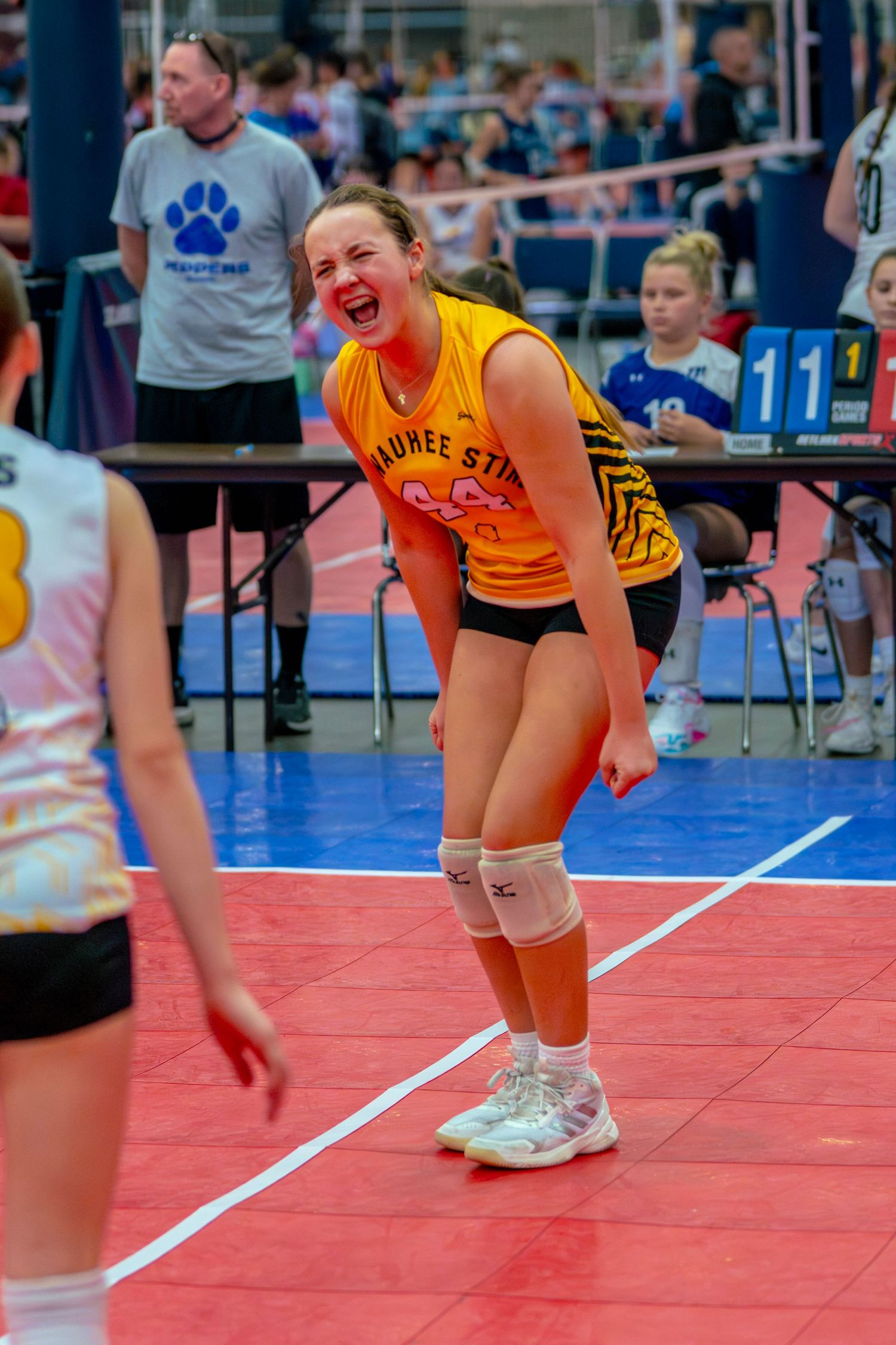 Young female volleyball player in orange jersey celebrates during a competitive indoor volleyball tournament match.