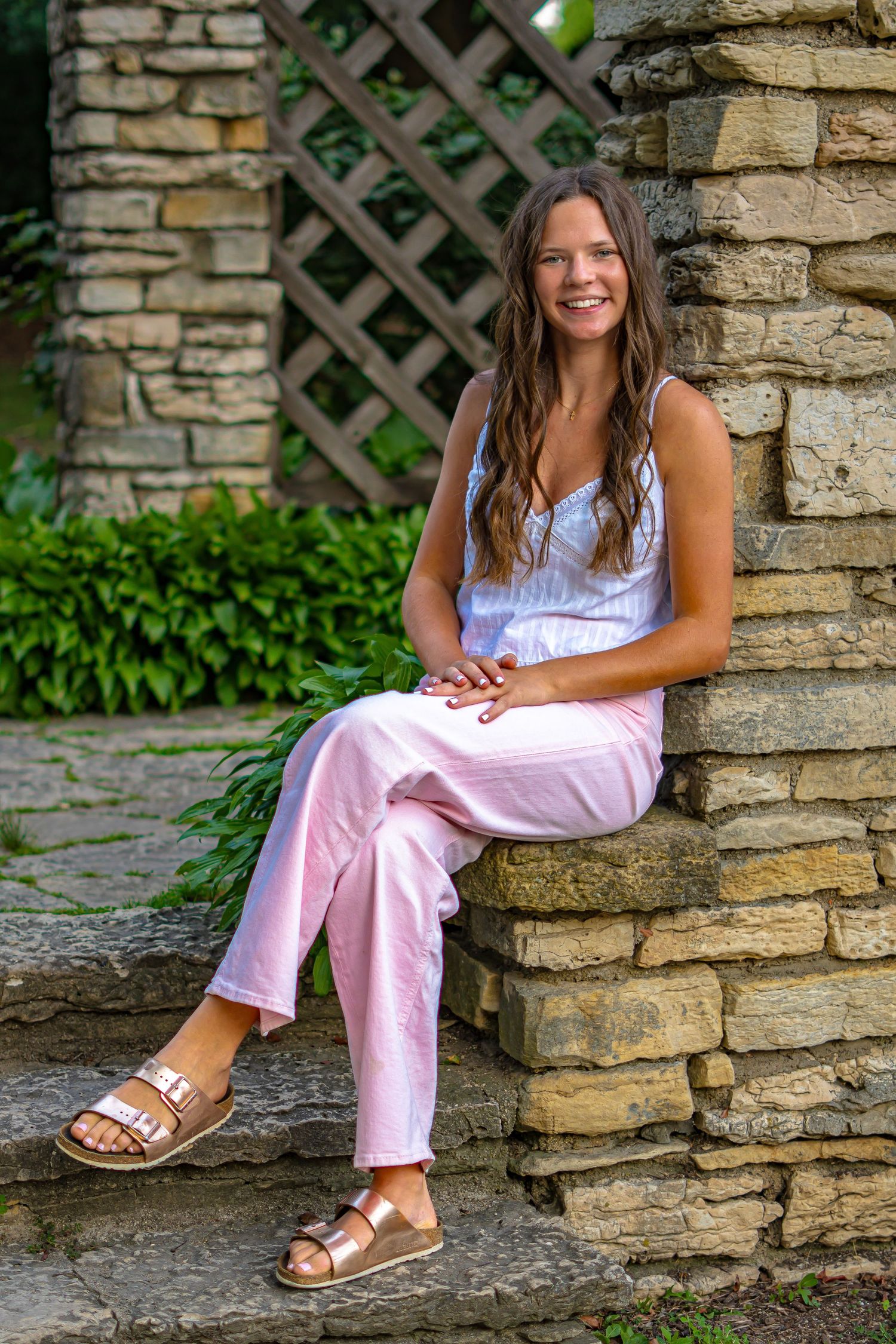 A senior outdoor photoshoot featuring someone sitting on stone steps wearing white and pink summer attire.