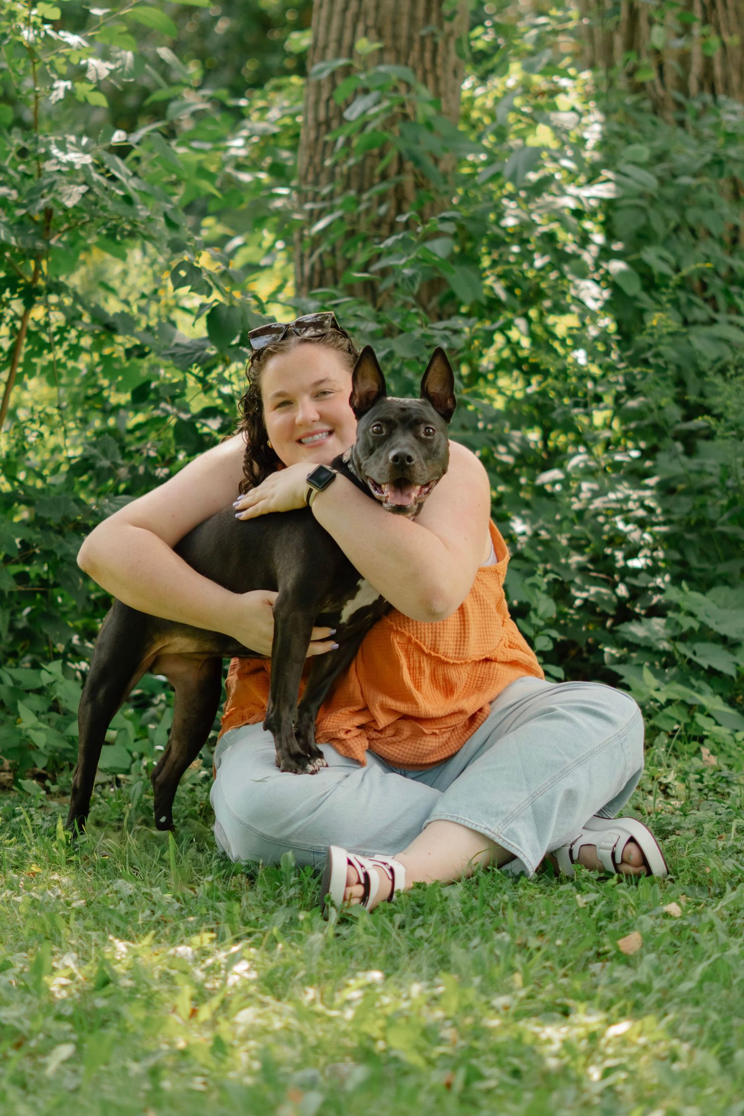 Child playing and cuddling with gray pit bull dog in lush green garden setting.