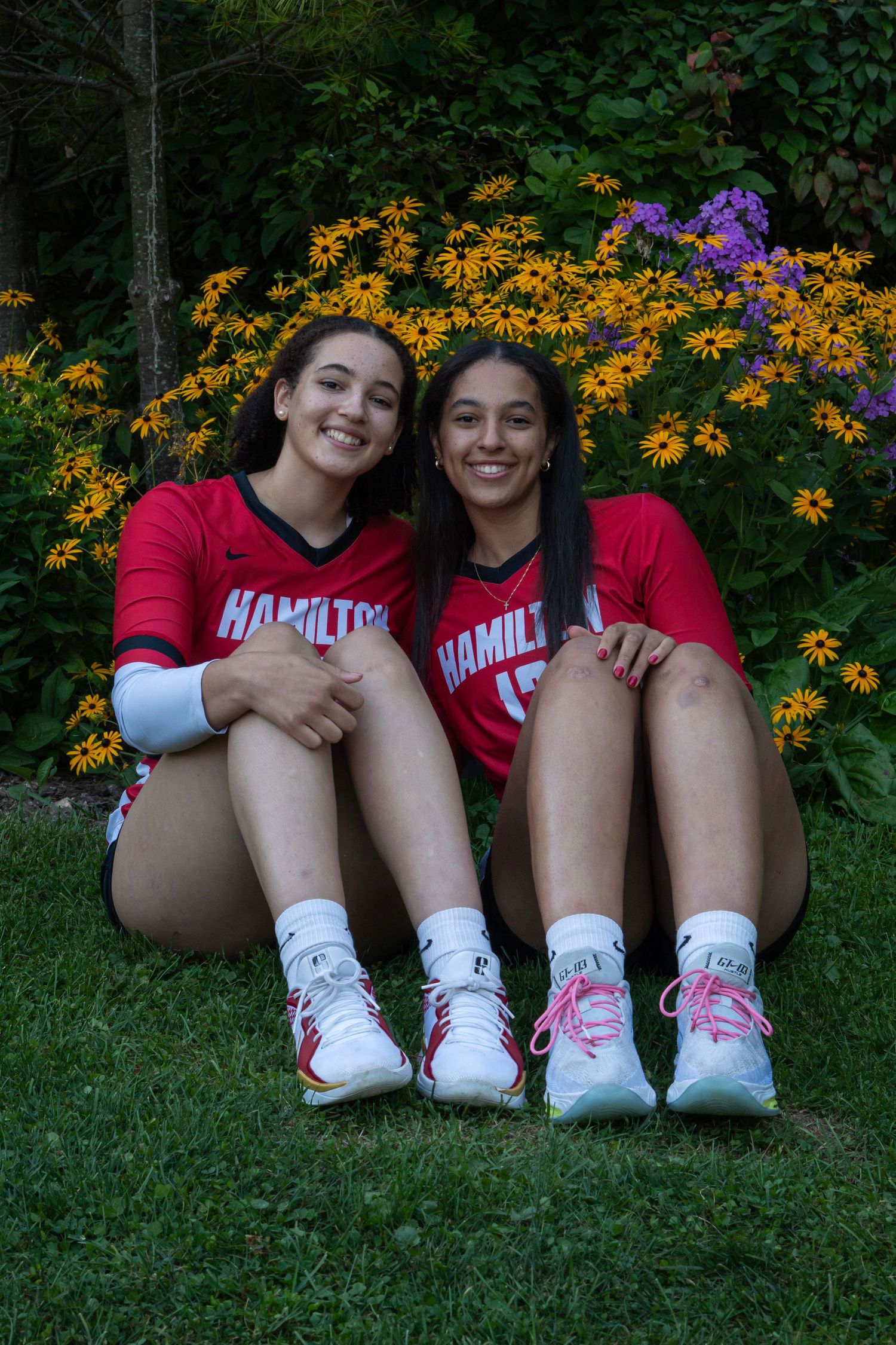 Team members in red uniforms sitting together showing off matching sneakers near garden.
