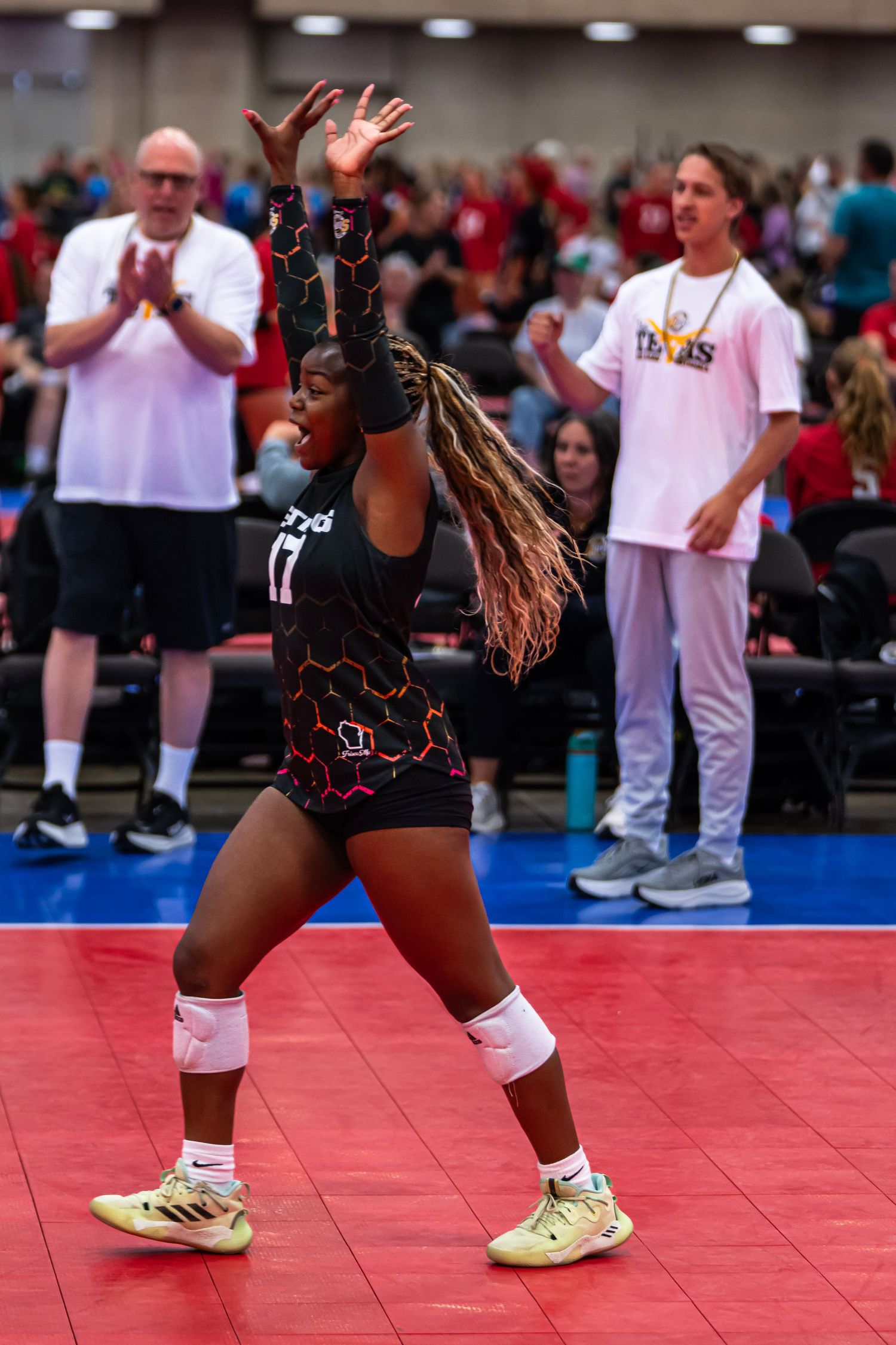 Players in black uniforms position themselves on a red court during a volleyball match.