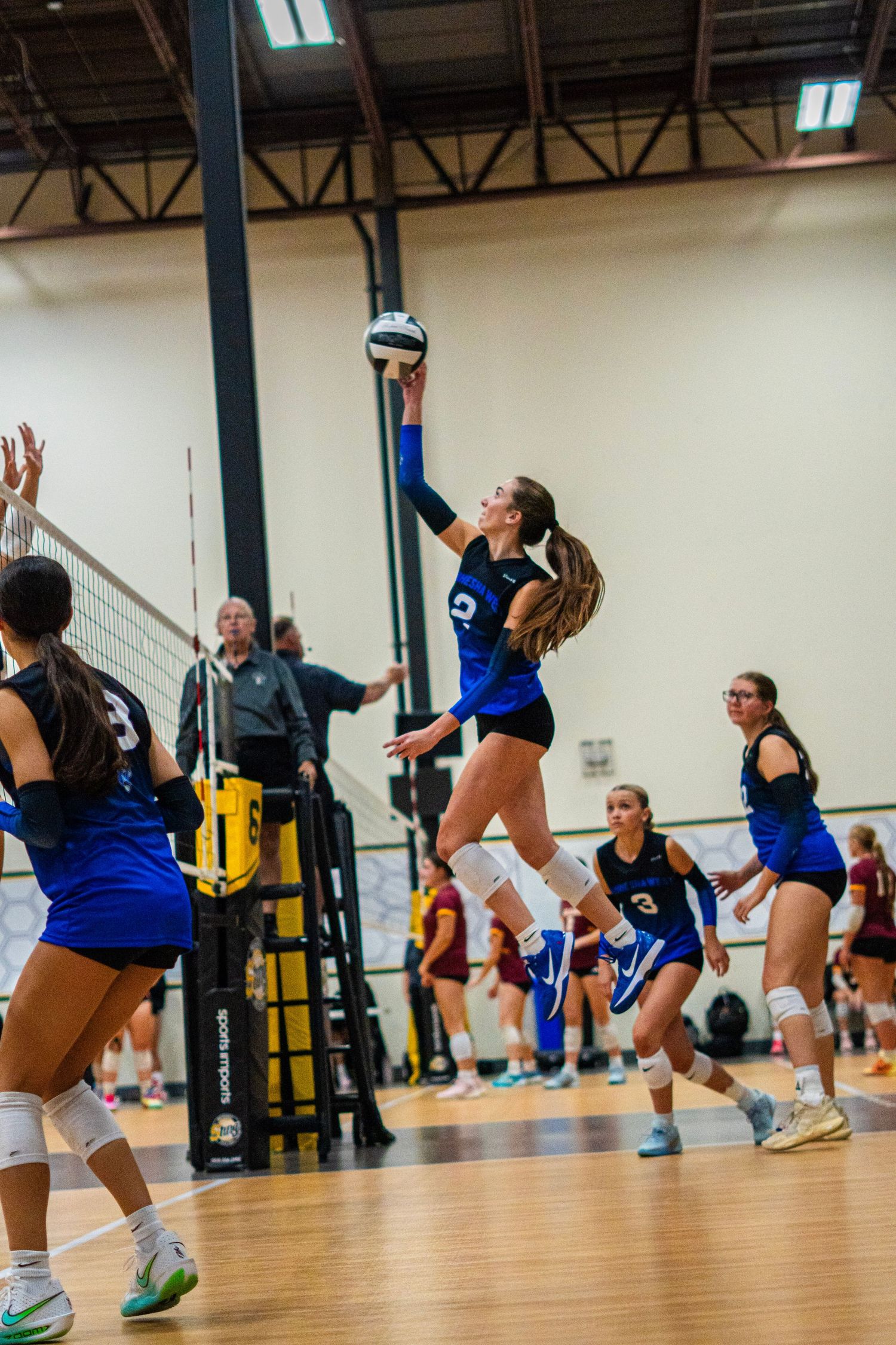 Volleyball team members jumping and positioning during active gameplay.