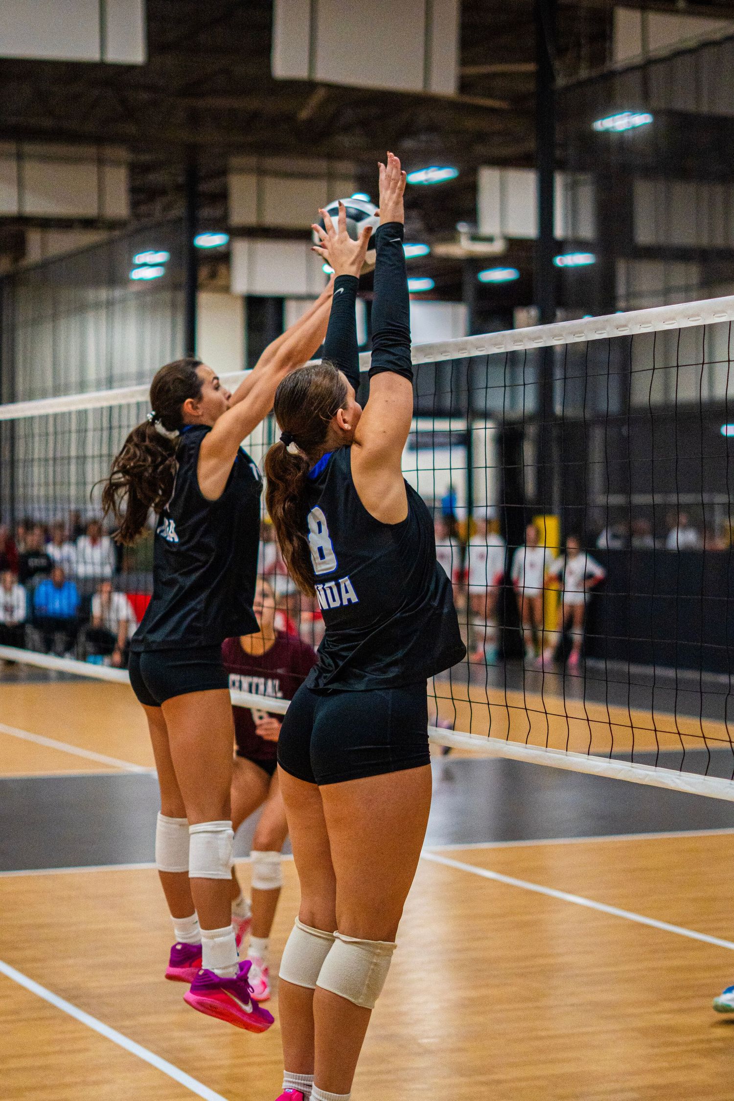 Indoor volleyball players practicing setting drills near the net.