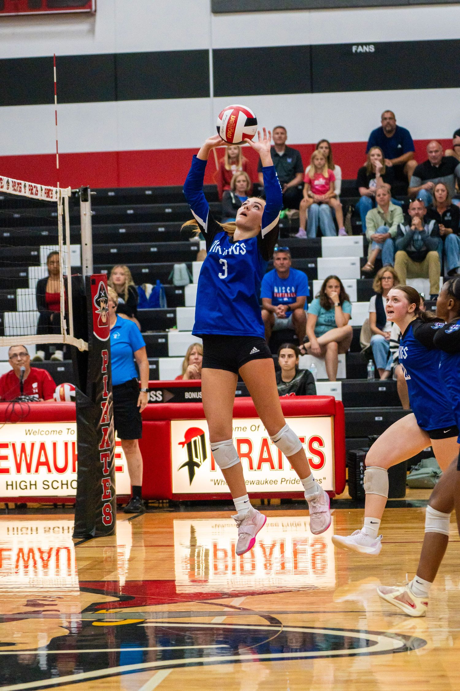 Volleyball players jump and position themselves during game action on home court.