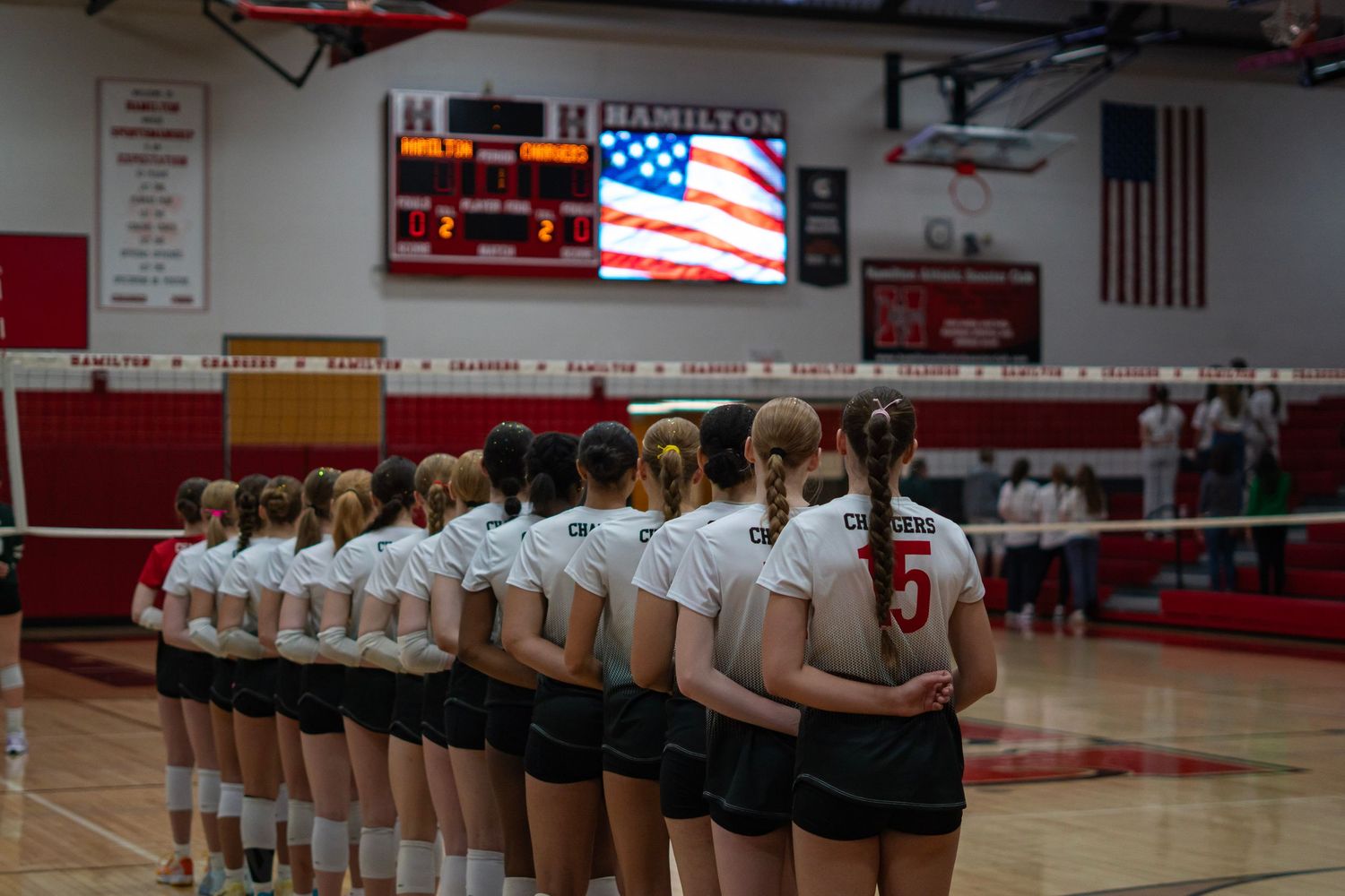 Volleyball team lined up on court during the national anthem.