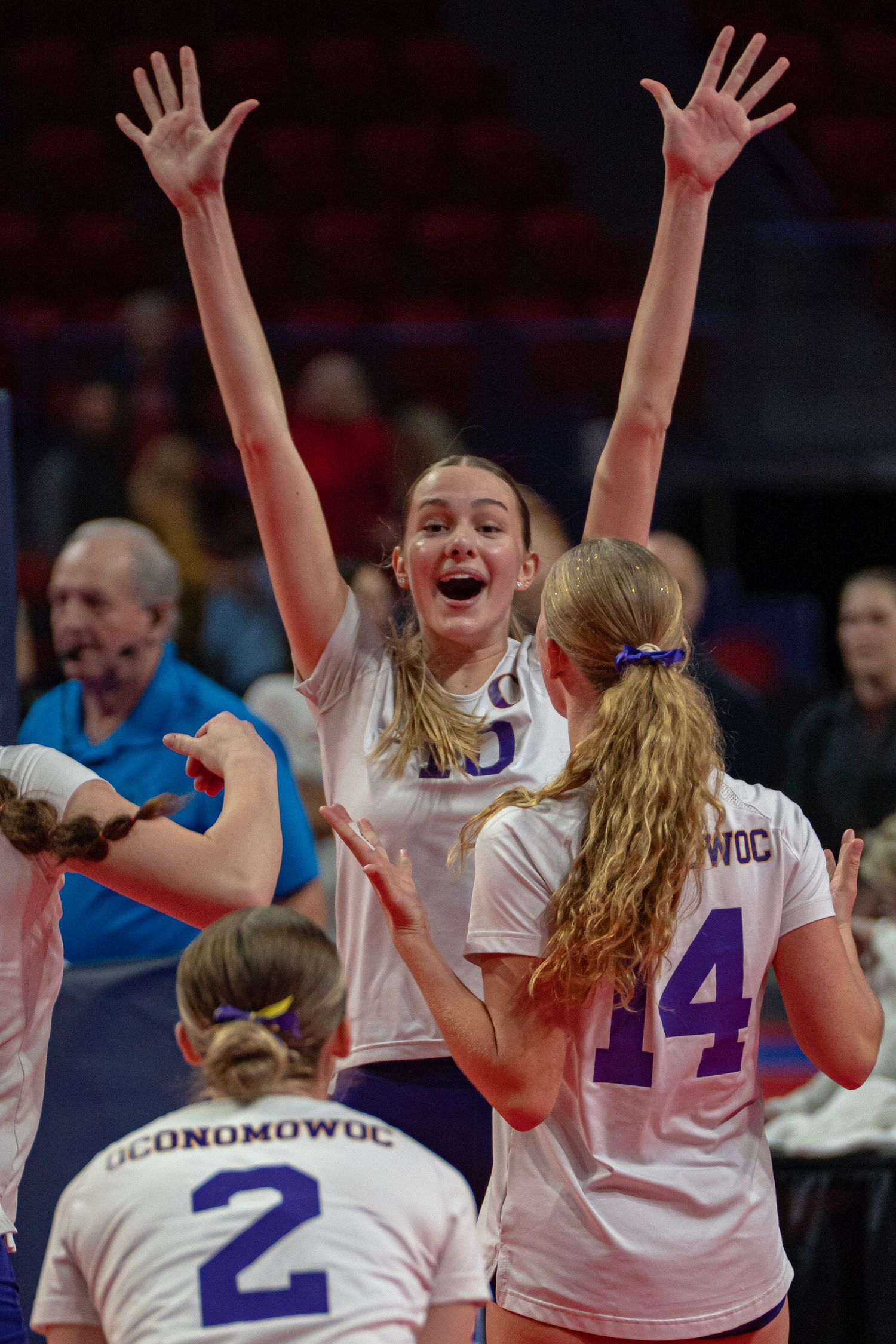 Volleyball players in white jerseys celebrate with raised arms during an exciting match moment.