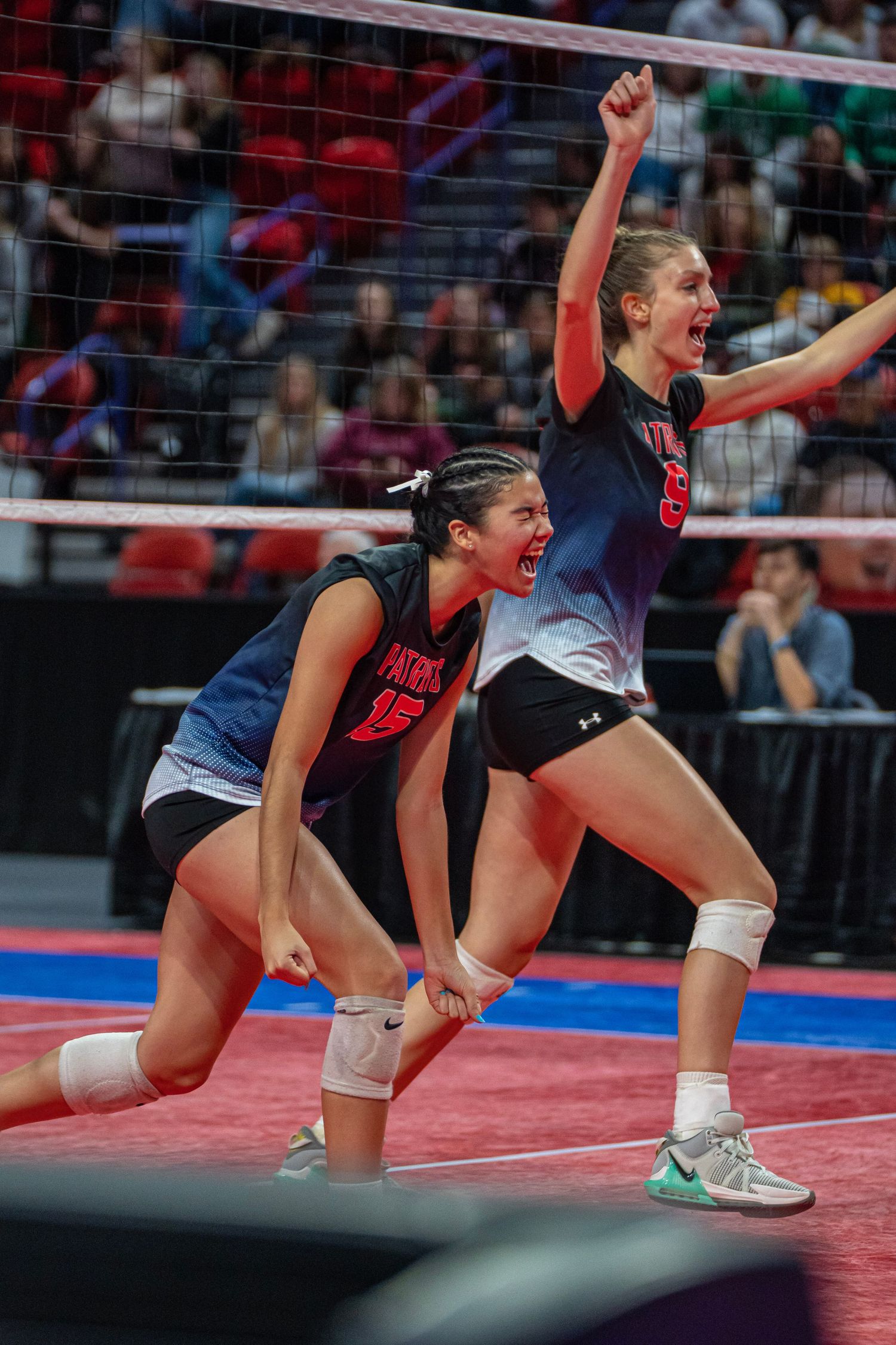 Two volleyball players celebrate enthusiastically near the net during an indoor tournament match.
