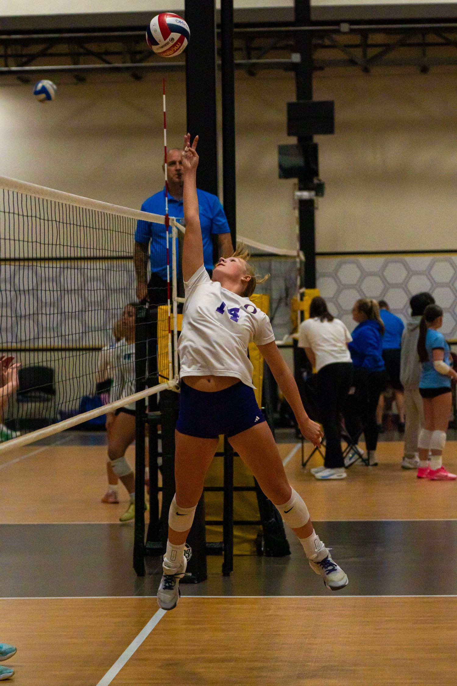 Indoor volleyball players making defensive plays near the net during competitive match.