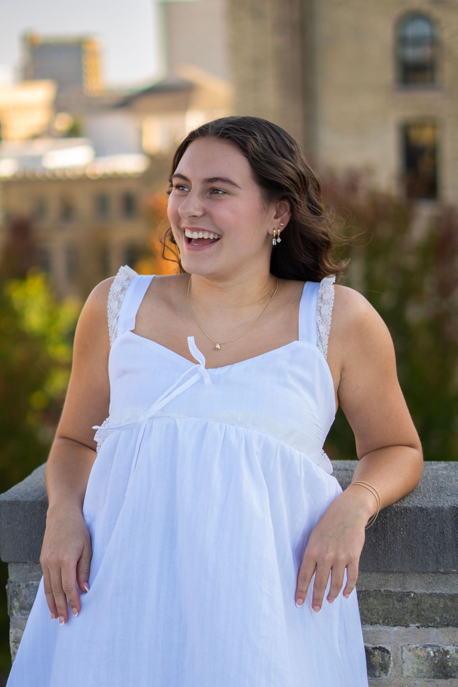 A person in a white sleeveless dress sits on a stone wall outdoors, shown in a series of candid poses.