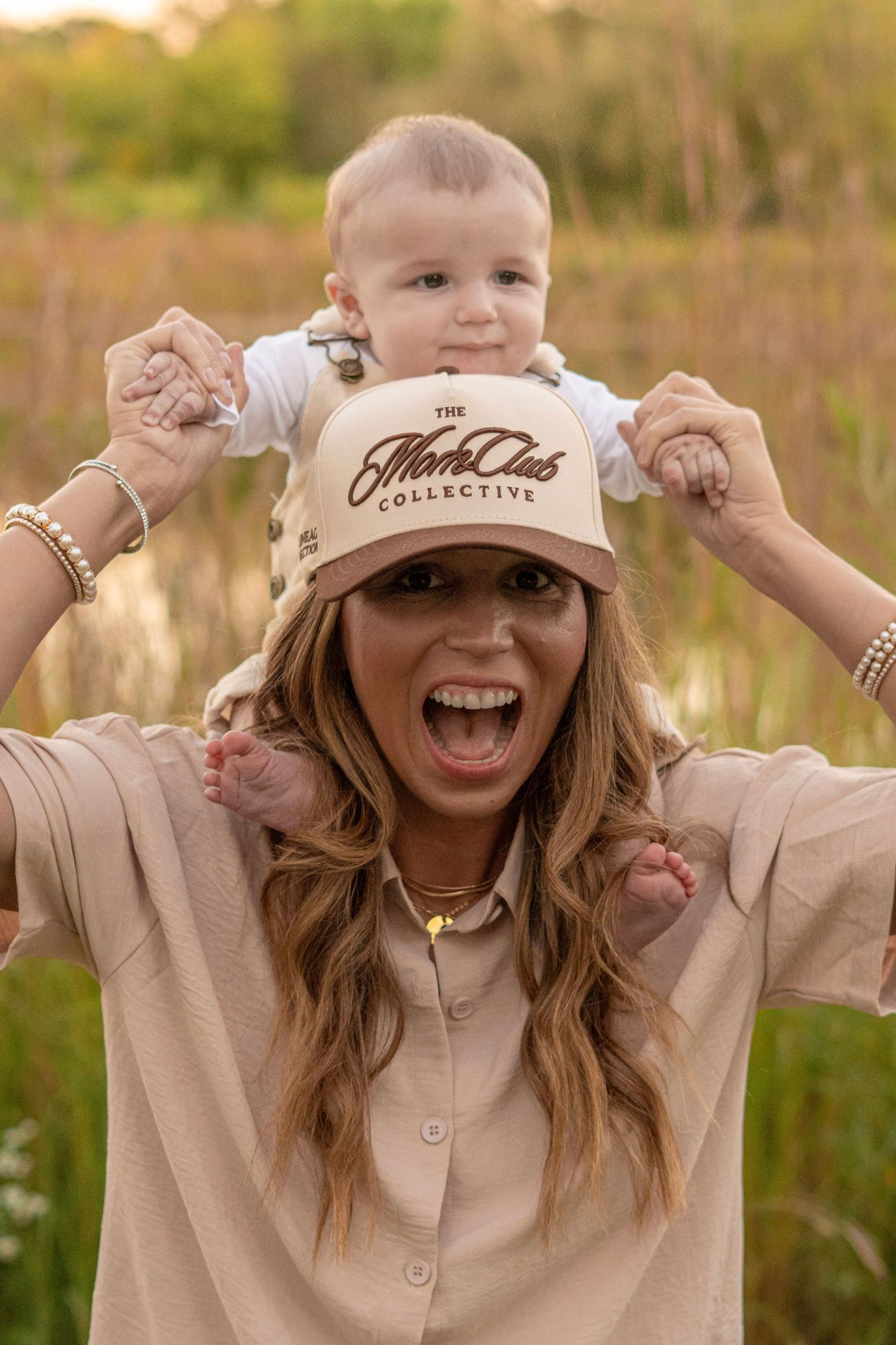 Person in beige outfit and cap shows excitement while posing outdoors at sunset.