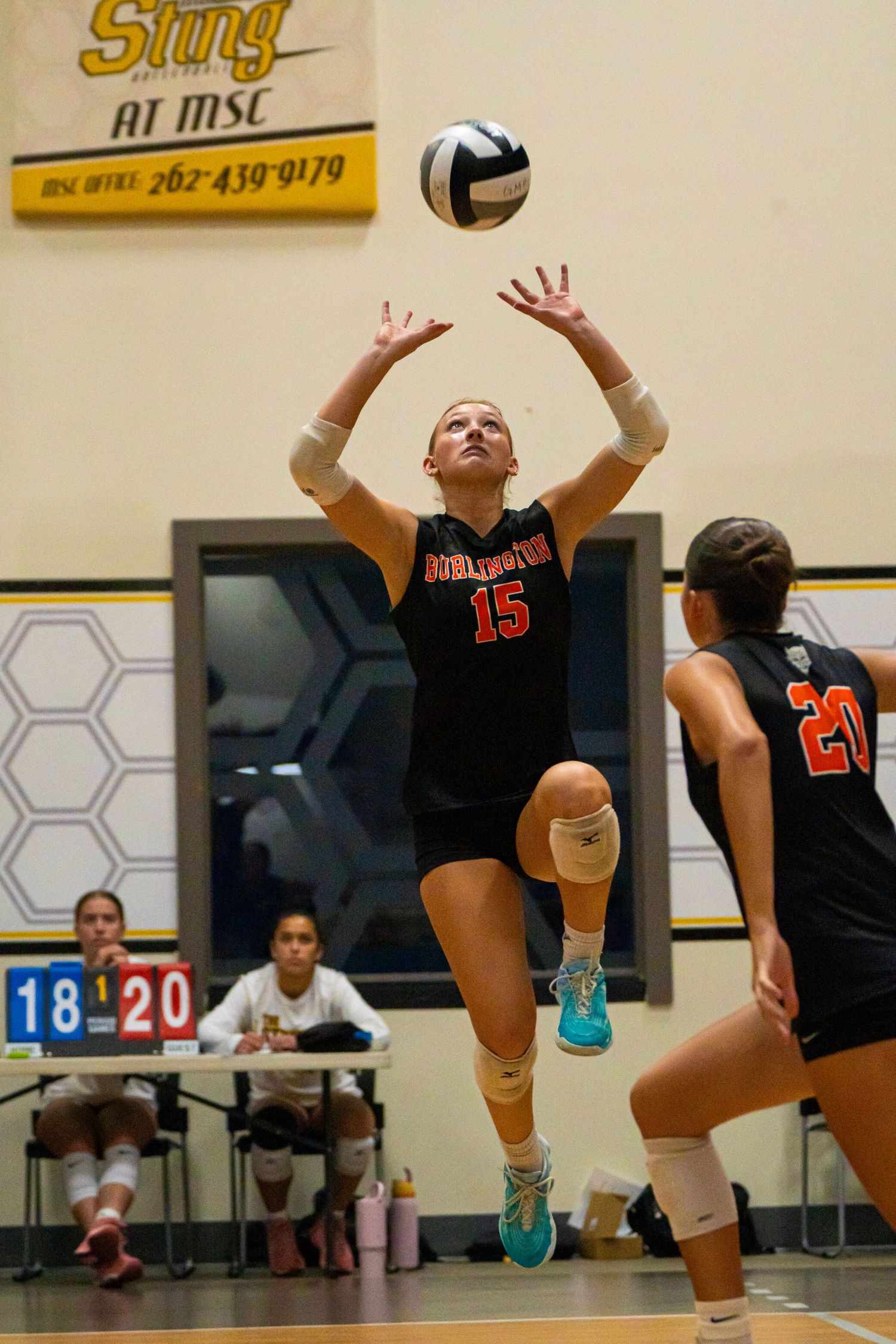 Players in black uniforms diving to save volleyball during indoor match.