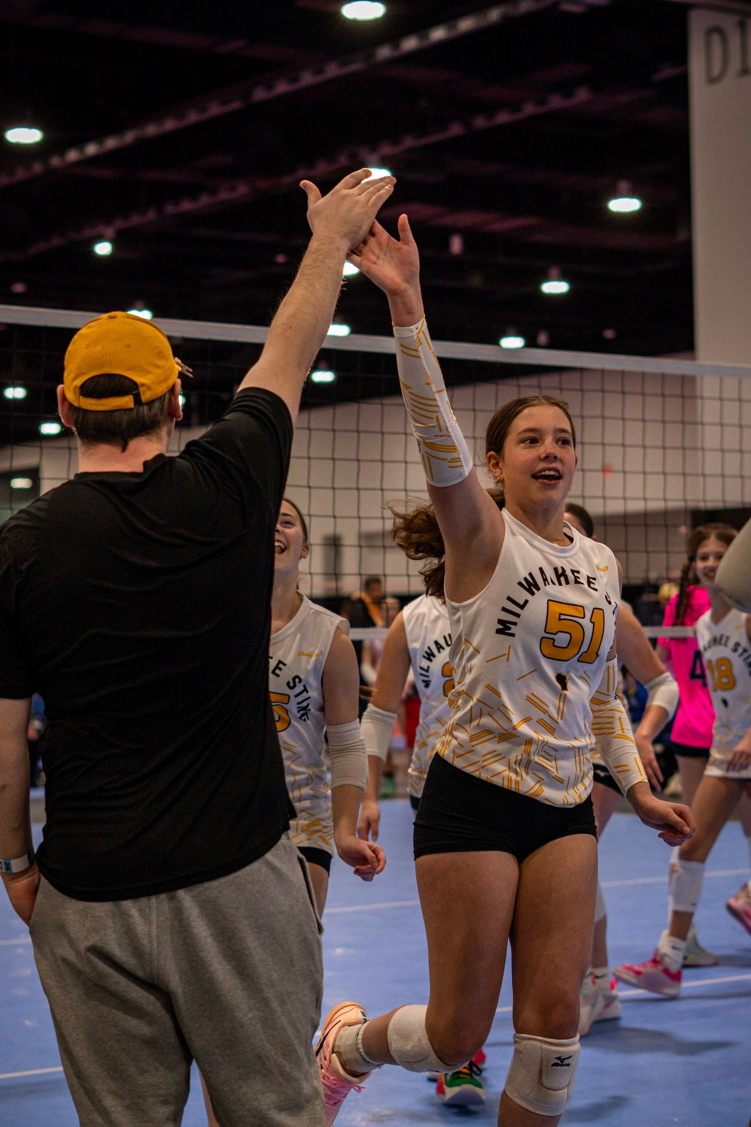 Milwaukee volleyball player #51 high-fives coach after match at indoor tournament.