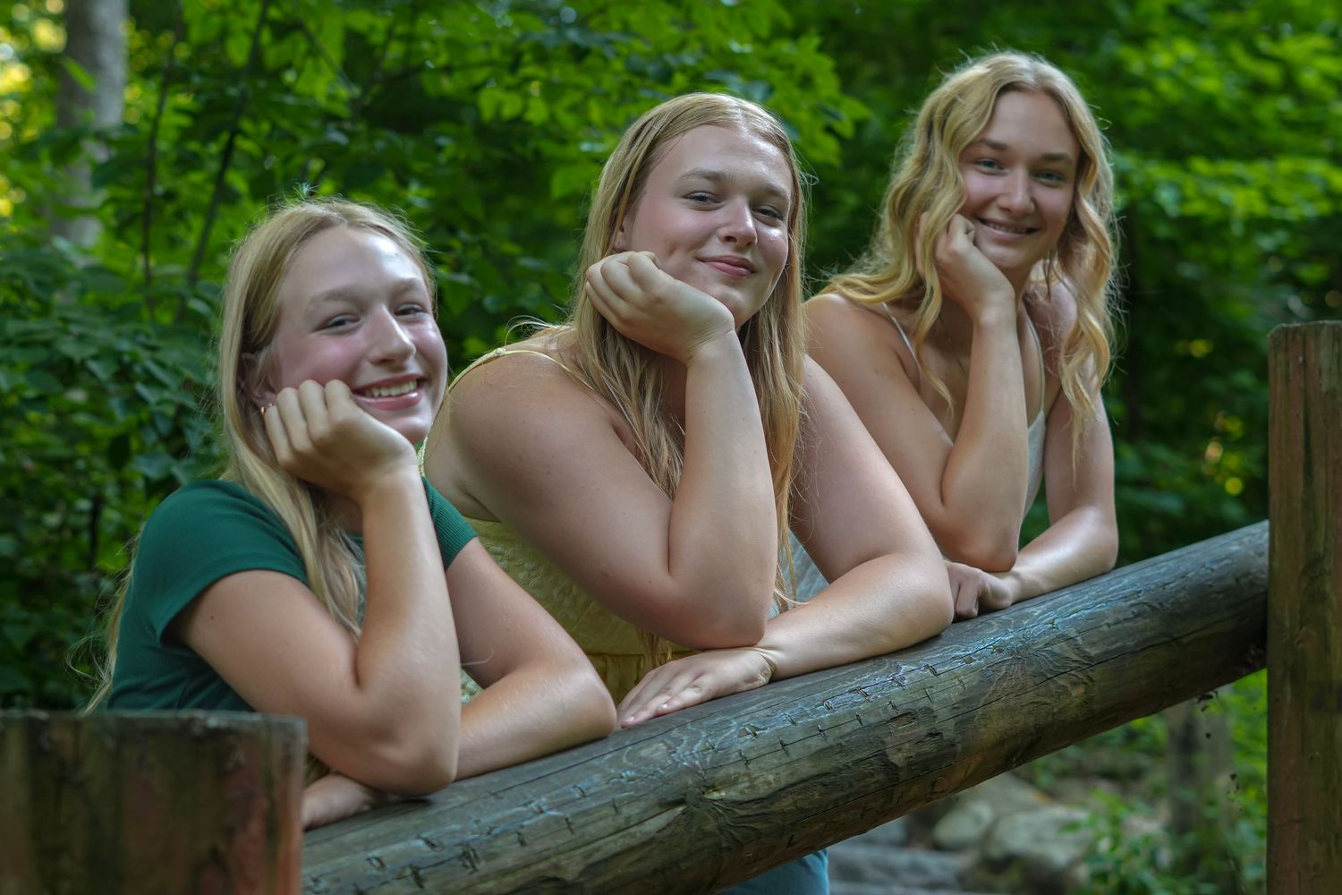 Friends share laughter while relaxing on a wooden log in a lush forest setting.