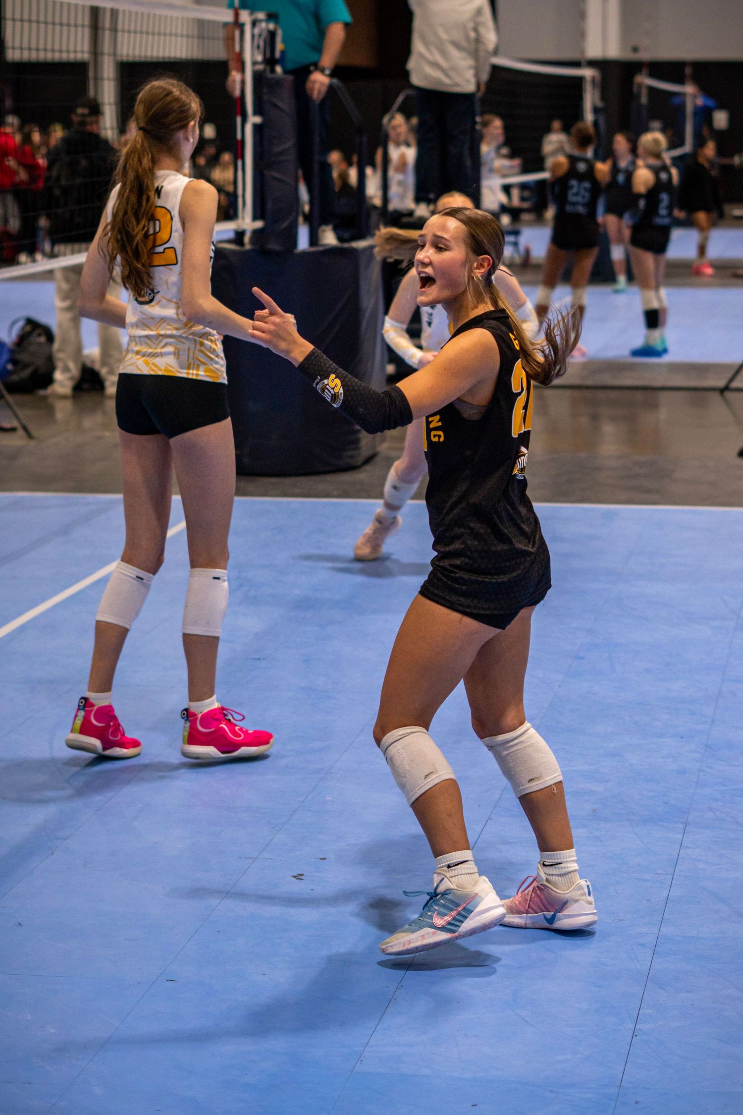 Young female volleyball players celebrate on blue court in black uniforms during indoor tournament match.