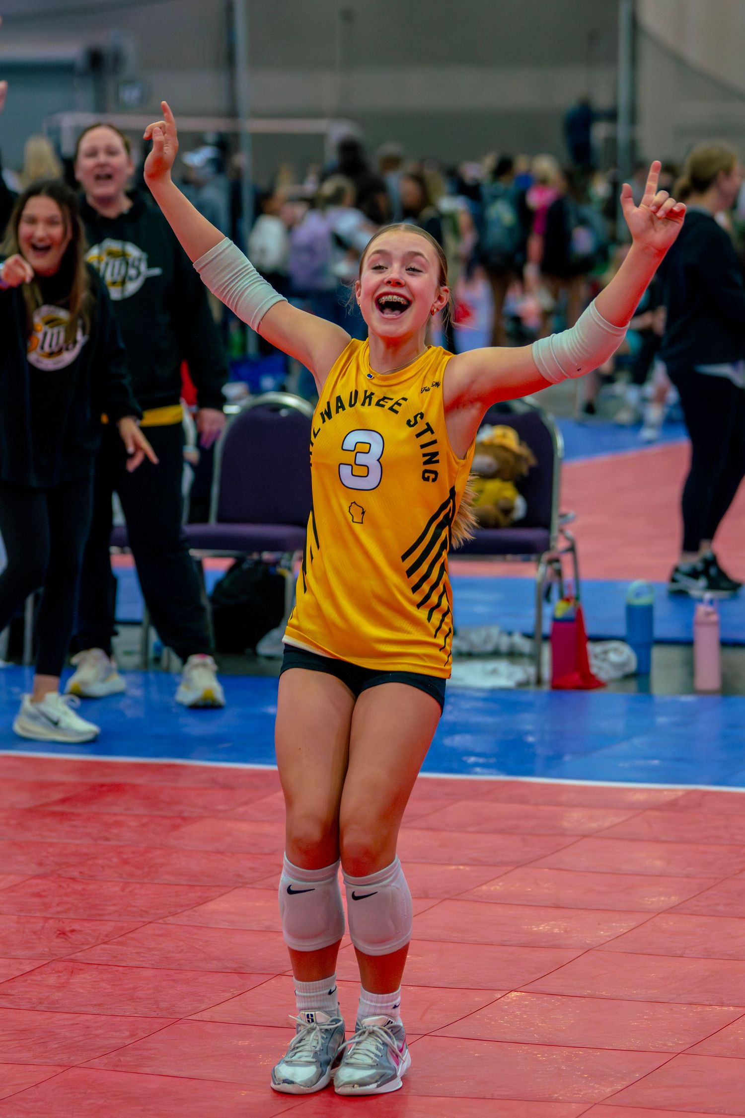 Young volleyball player in yellow jersey number 3 celebrates victory with arms raised at indoor tournament.
