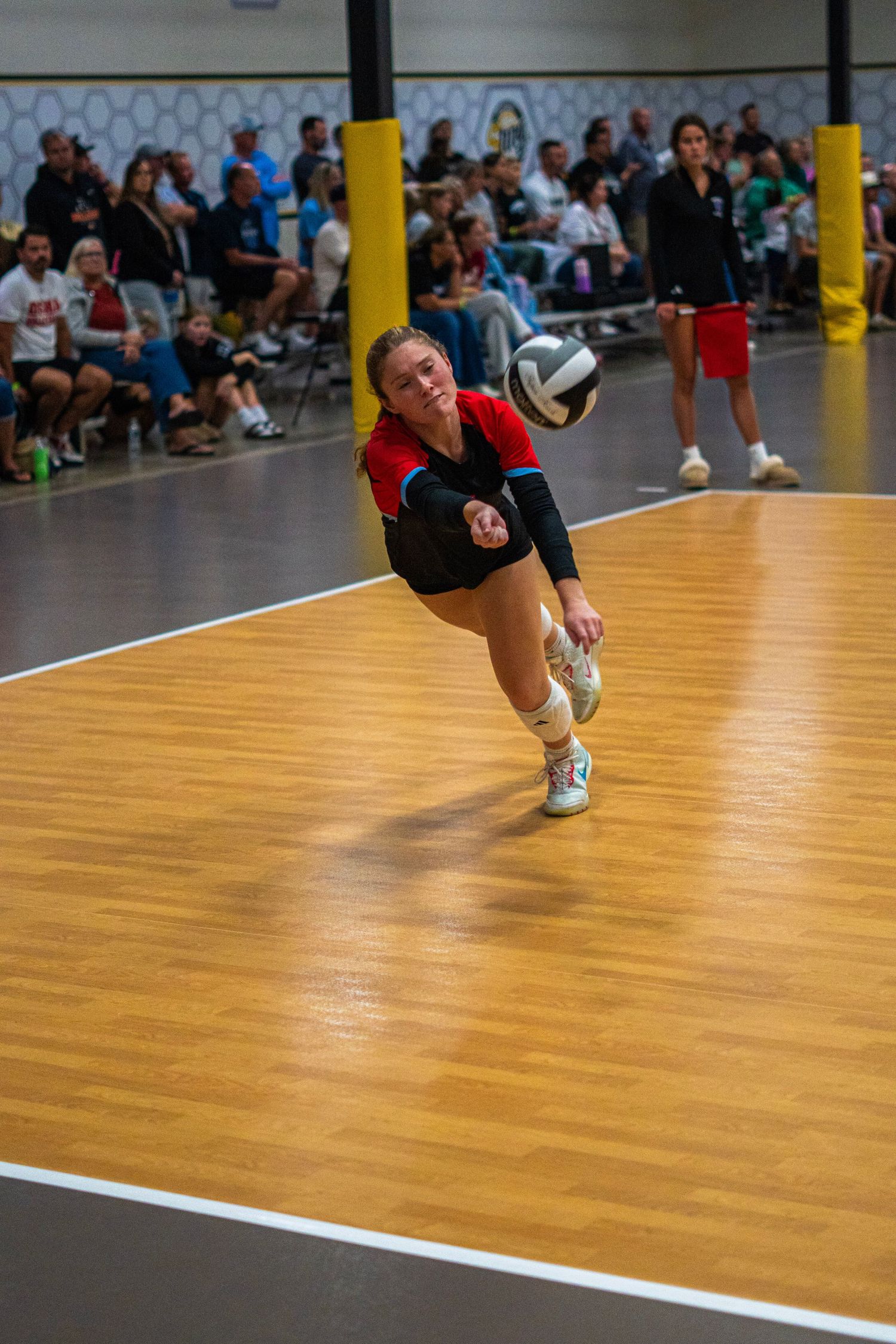 Player executing dramatic diving save on wooden volleyball court during game.