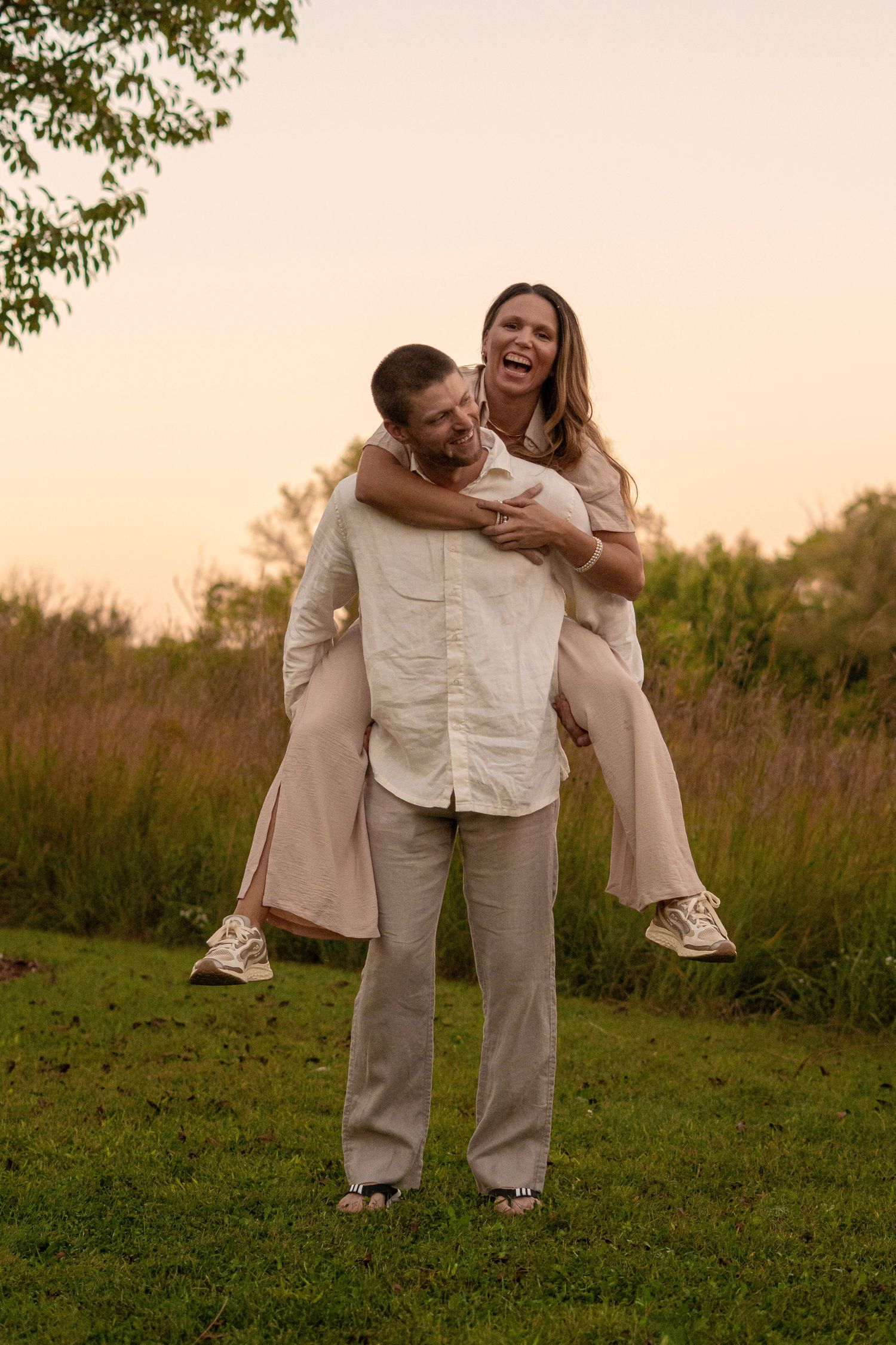Couple in neutral colored outfits share playful moment during sunset photo session.