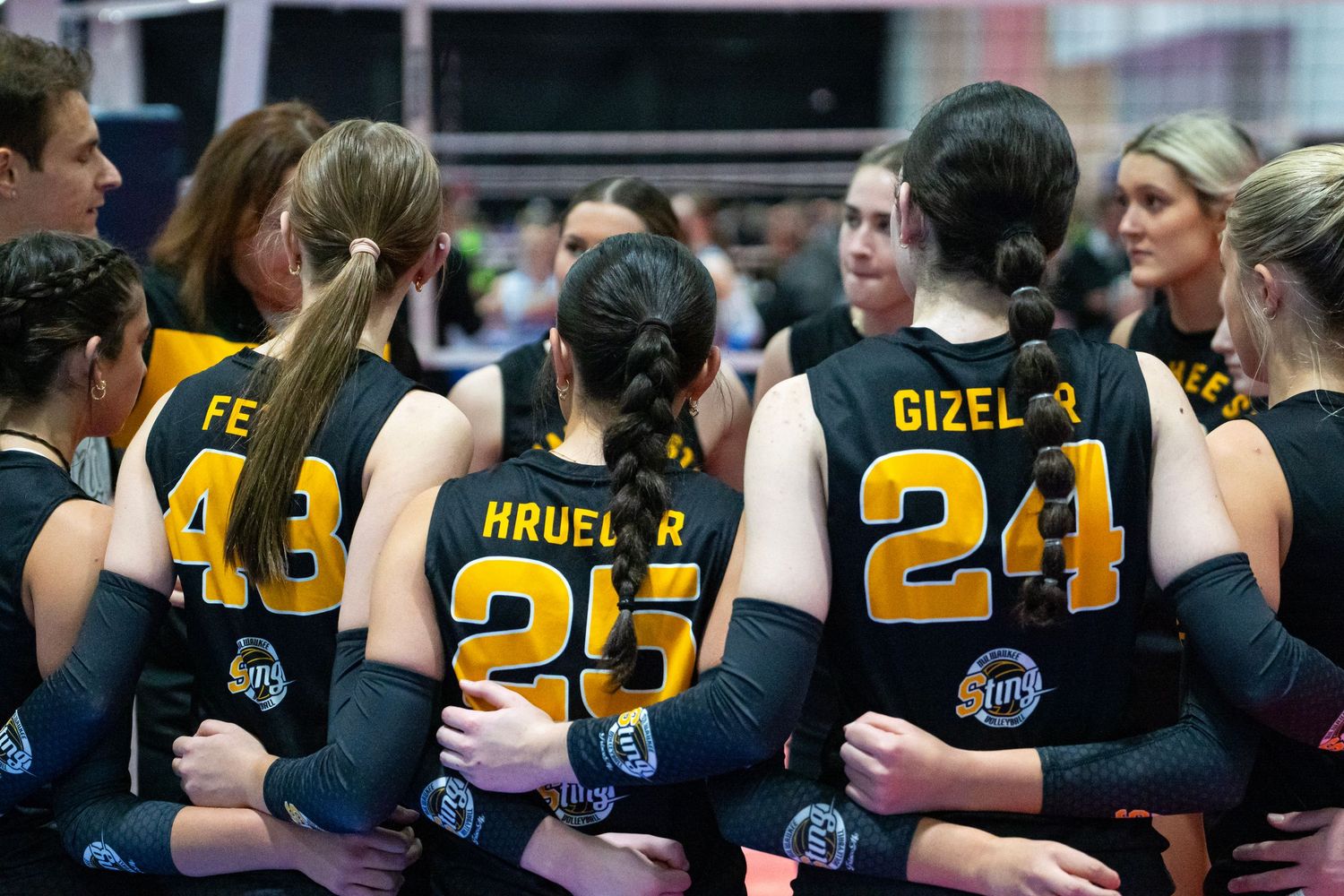 Female volleyball team huddles together in black and gold uniforms with names Gizeler, Hrueler, and Fer visible.