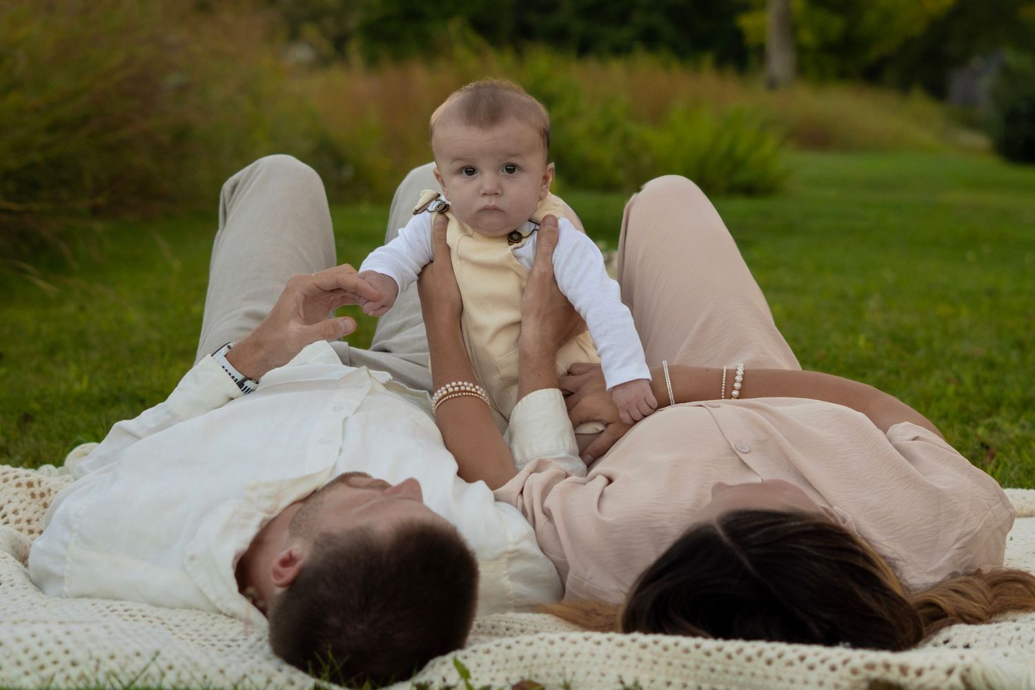 Family lying together on white blanket during outdoor photo session.