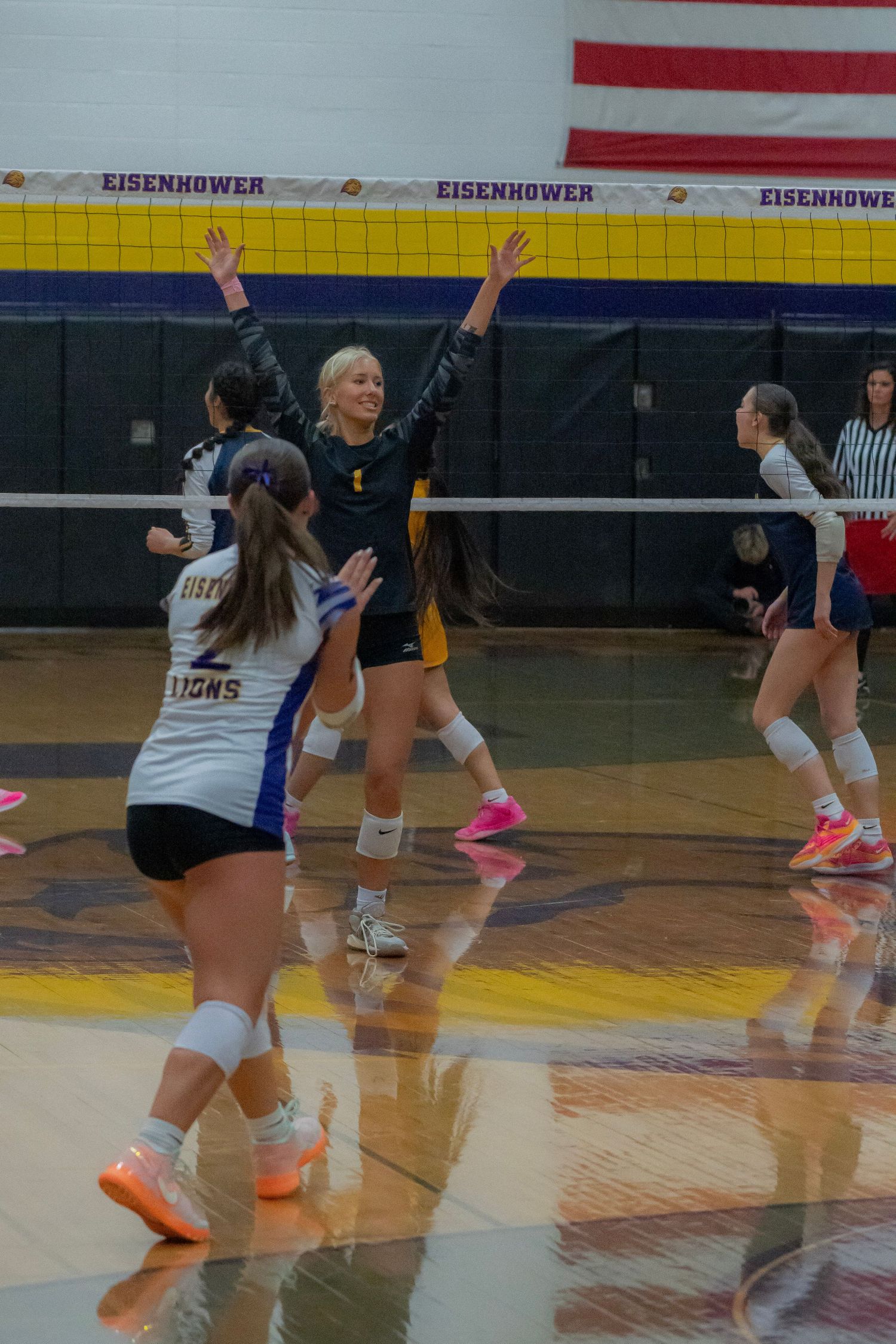 Volleyball players in black and white uniforms jump and move across a gymnasium court during an indoor match.