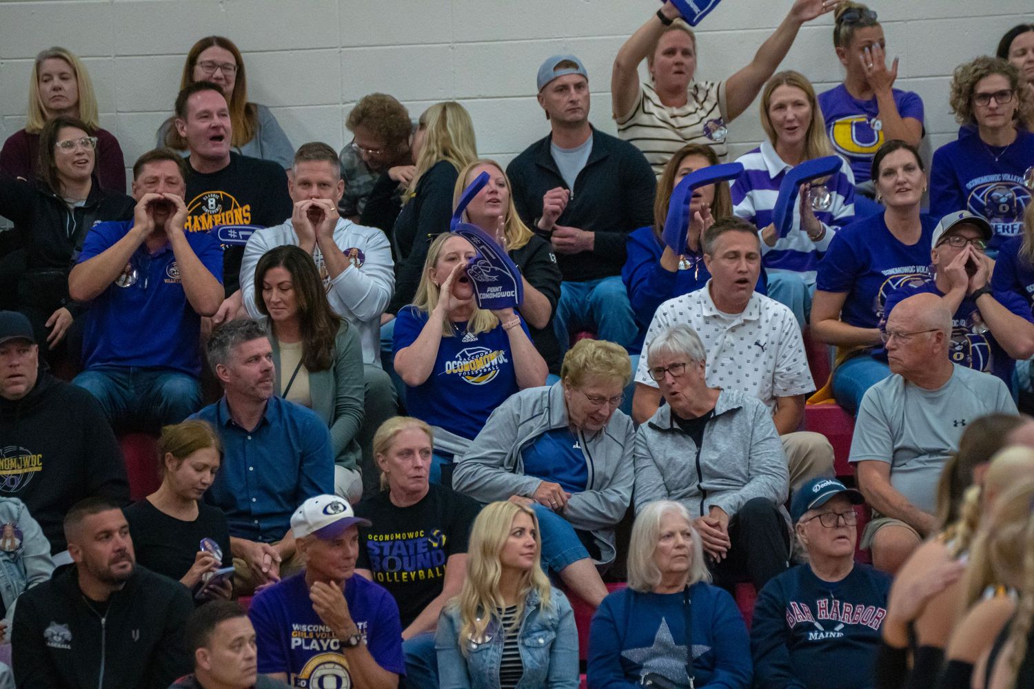 Engaged spectators watch intently from bleachers during a volleyball match.