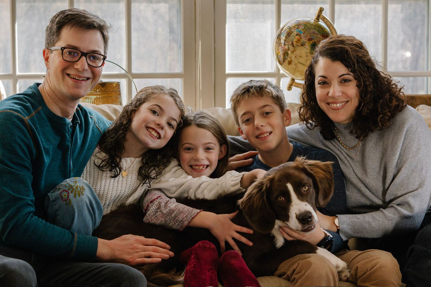 Happy family of four with a beagle dog posing together on a couch in a cozy living room.