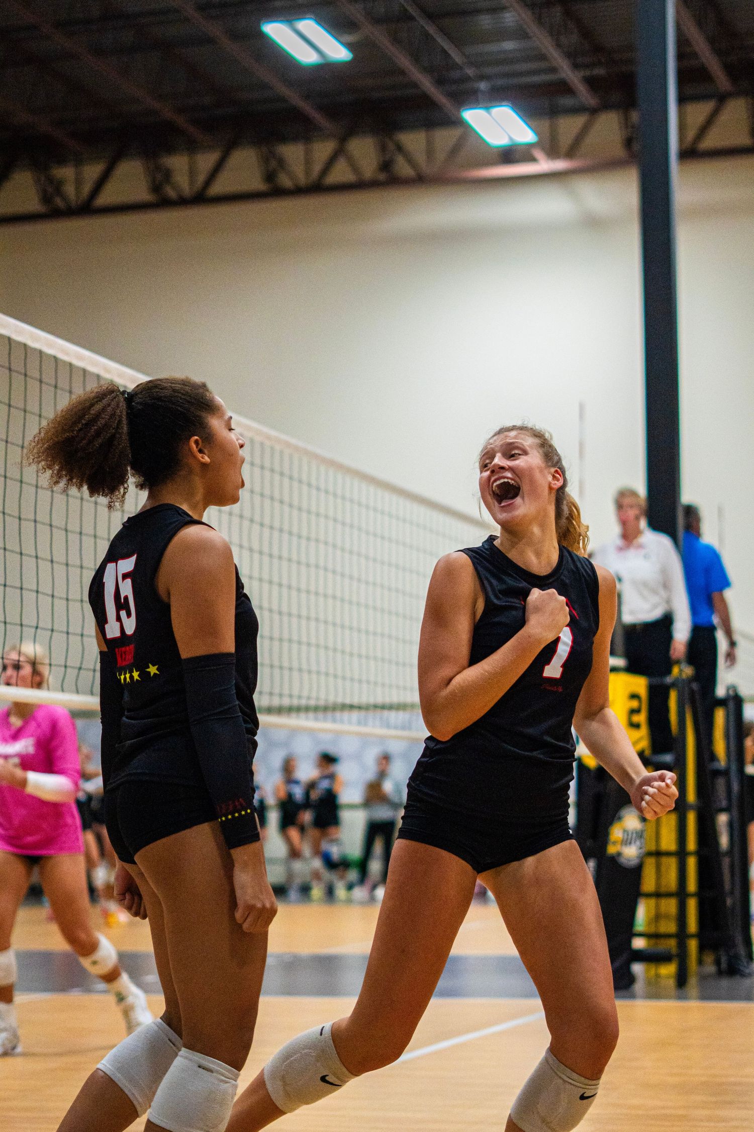 Volleyball players diving and stretching for ball during intense indoor game play.
