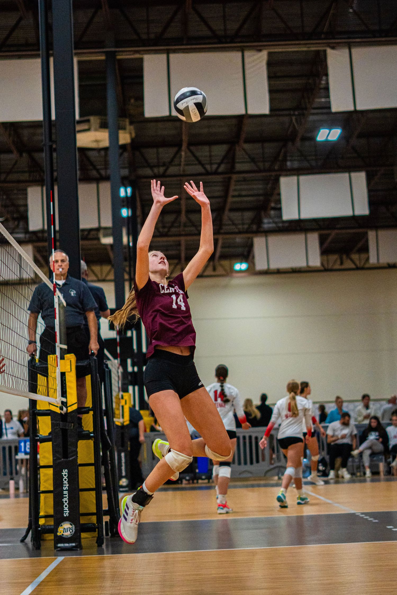 Volleyball players jumping at net during competitive indoor match play.
