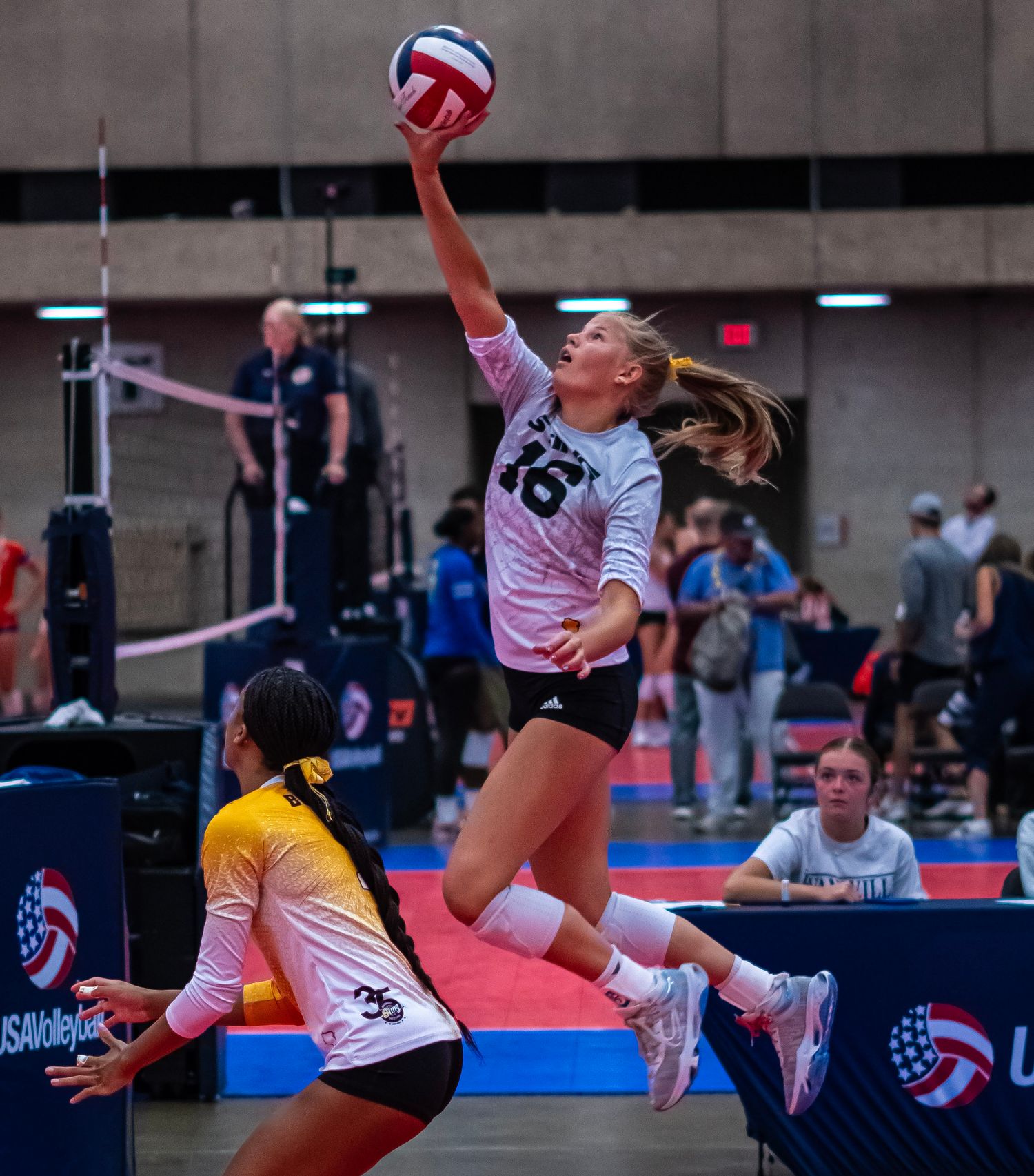 Volleyball players dive and jump for the ball during a competitive indoor match.