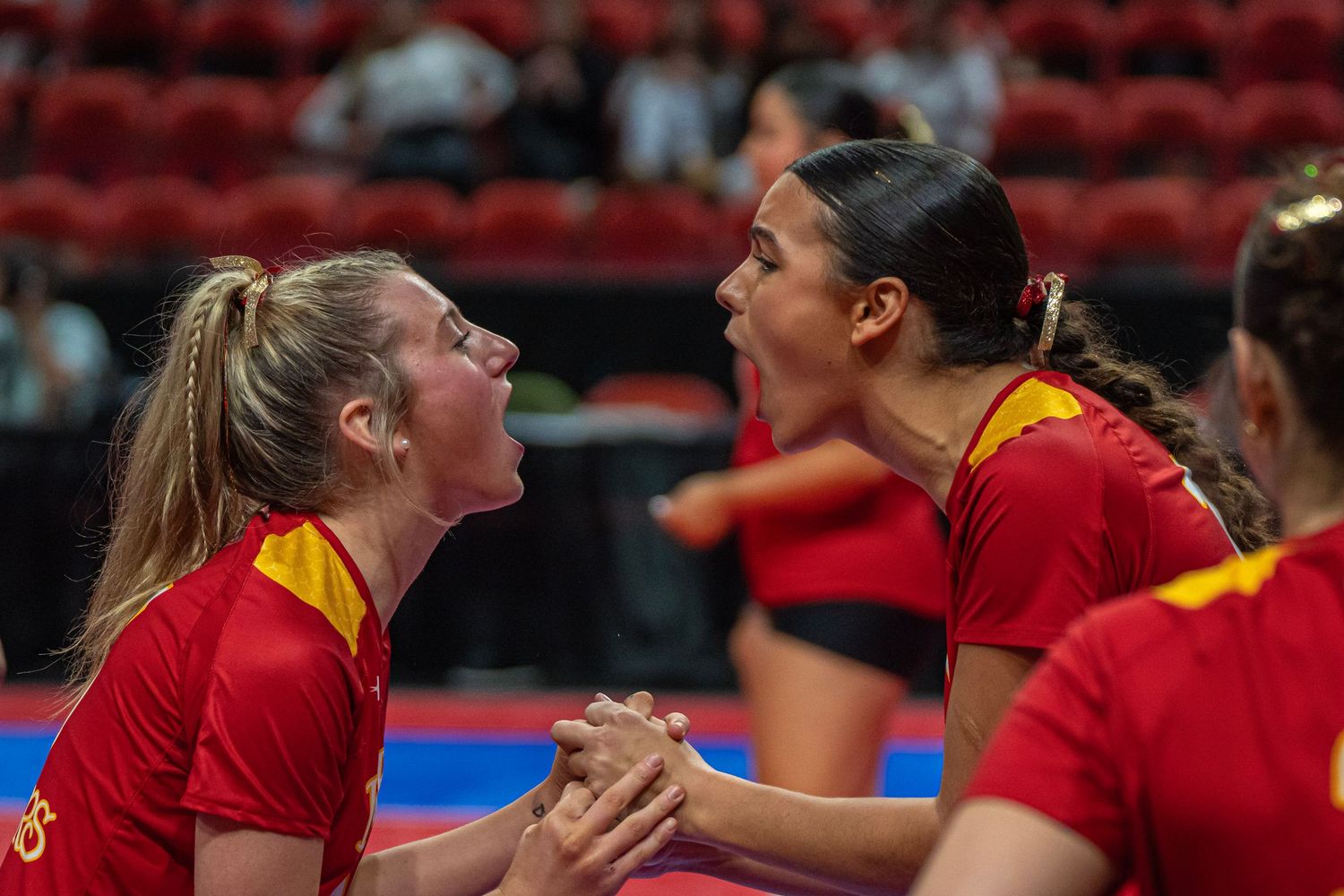 Two volleyball teammates in red uniforms celebrate with intense emotion during a match.