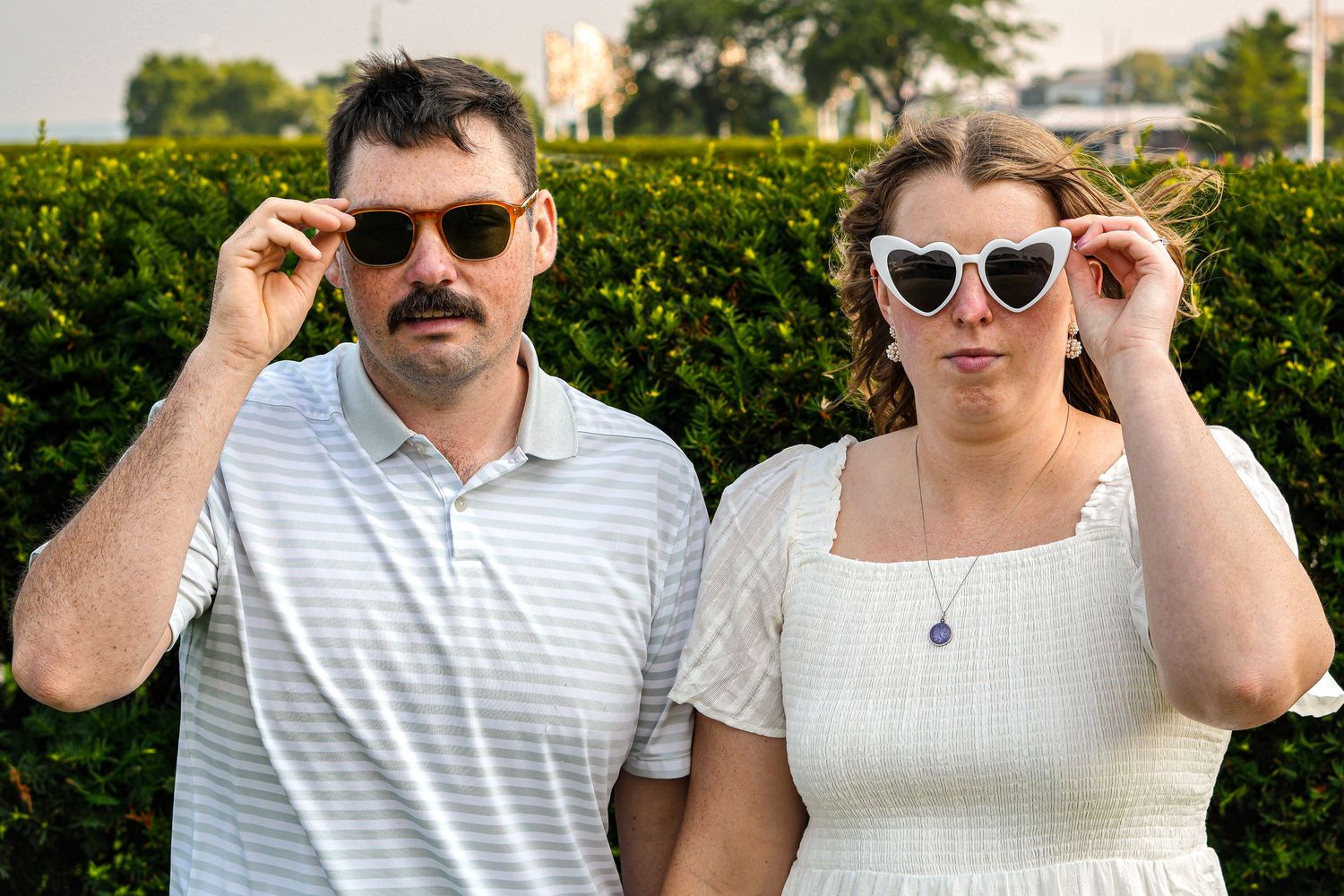 Couple in summer outfits pose with sunglasses at outdoor location.