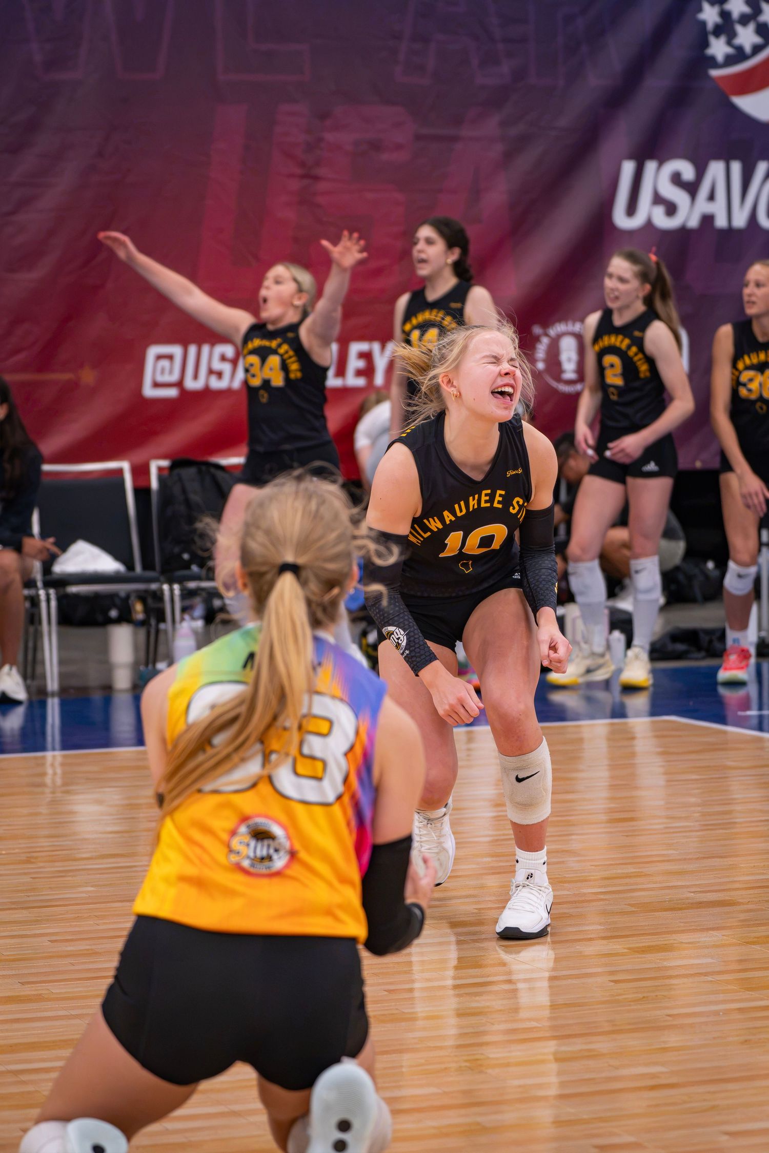 Milwaukee St. volleyball players celebrate enthusiastically during a USAV tournament match on an indoor court.