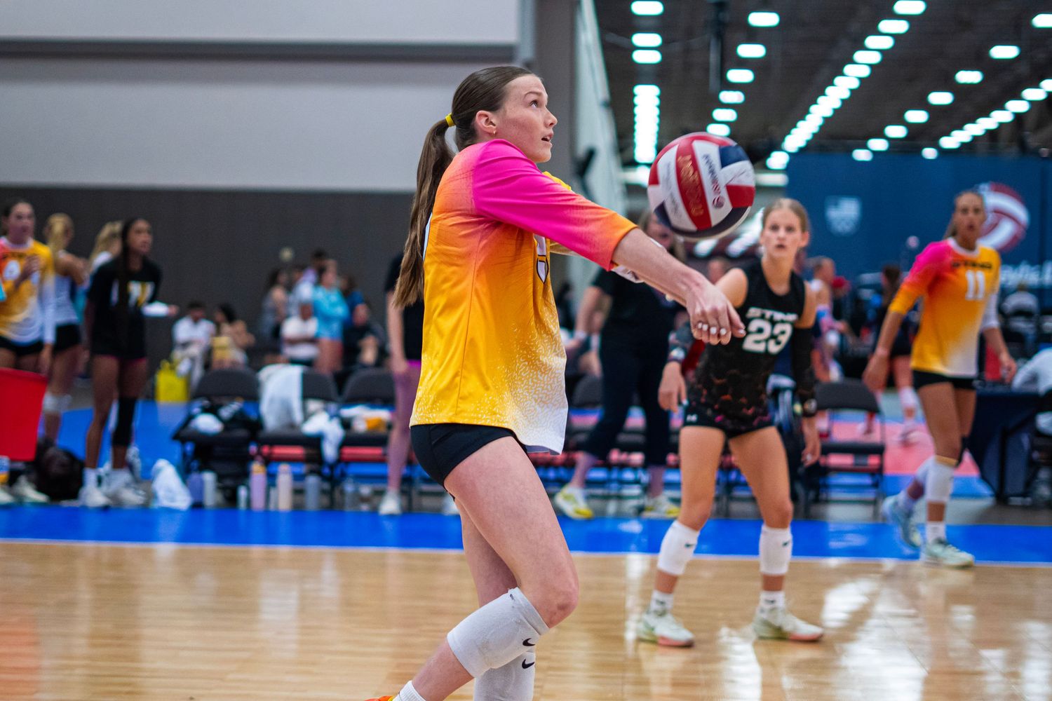 Athletes dive and stretch for the ball during an indoor volleyball tournament.