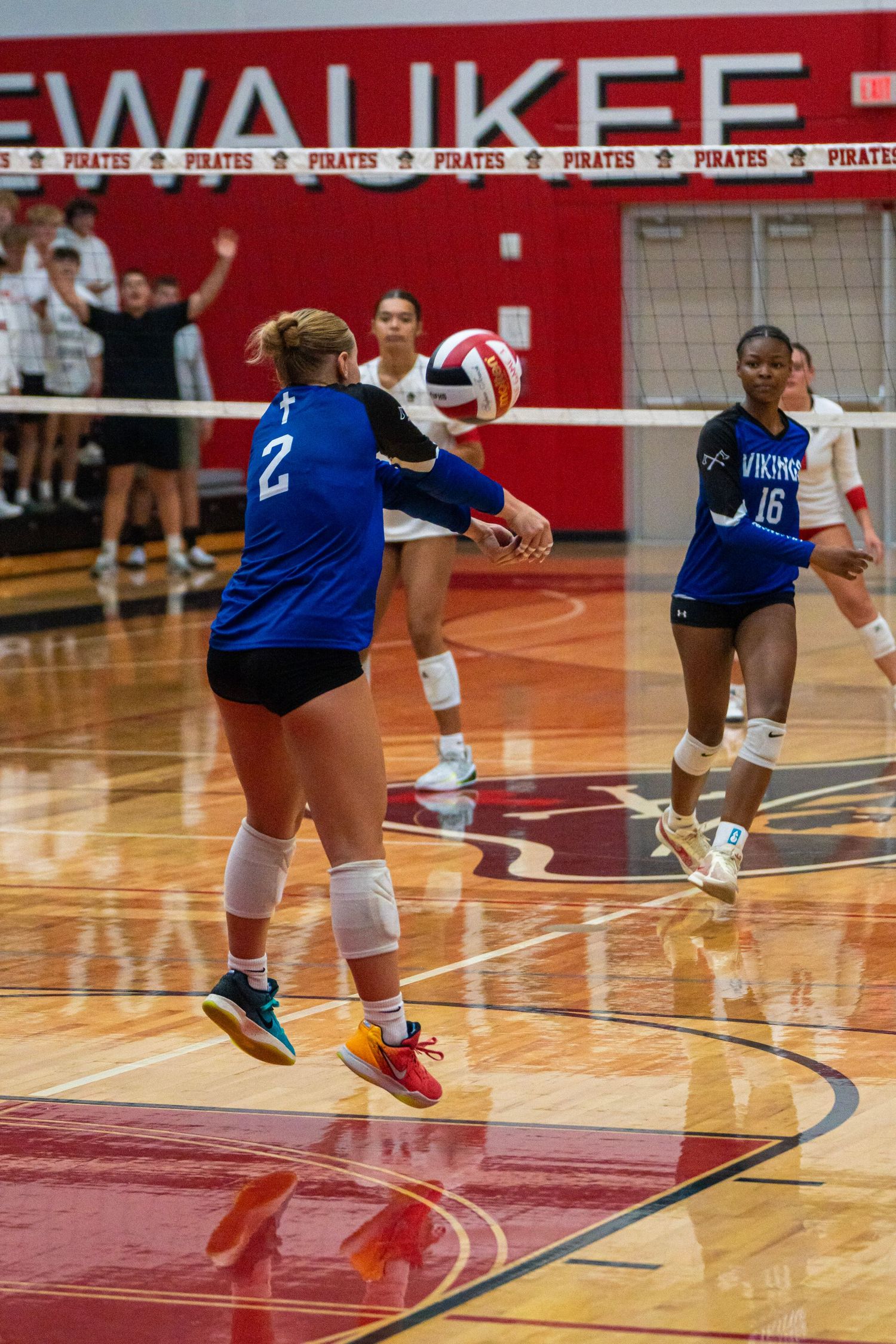 Players in blue uniforms dive for the ball on red gymnasium court.
