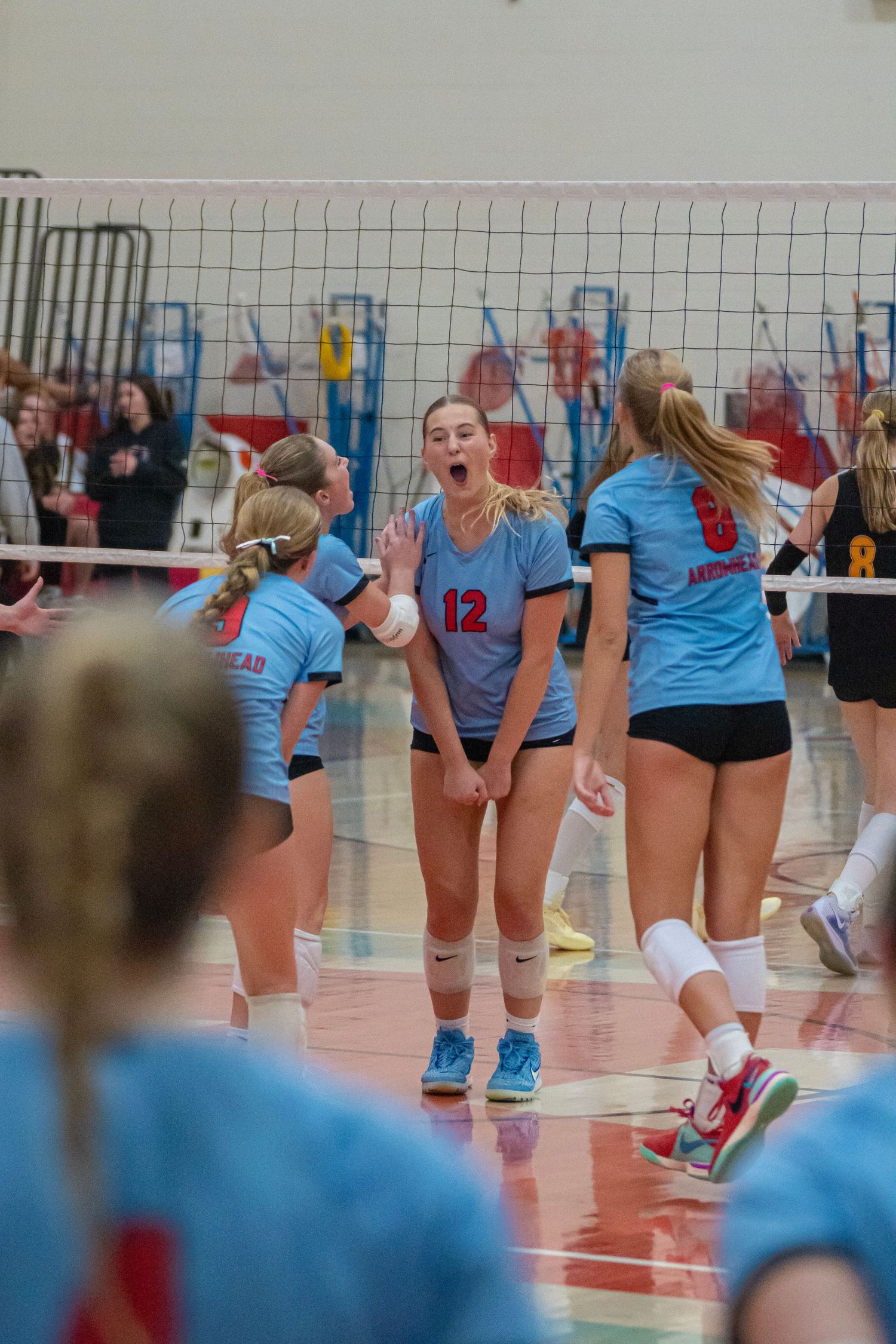 Volleyball team in light blue jerseys celebrates a point during a match.