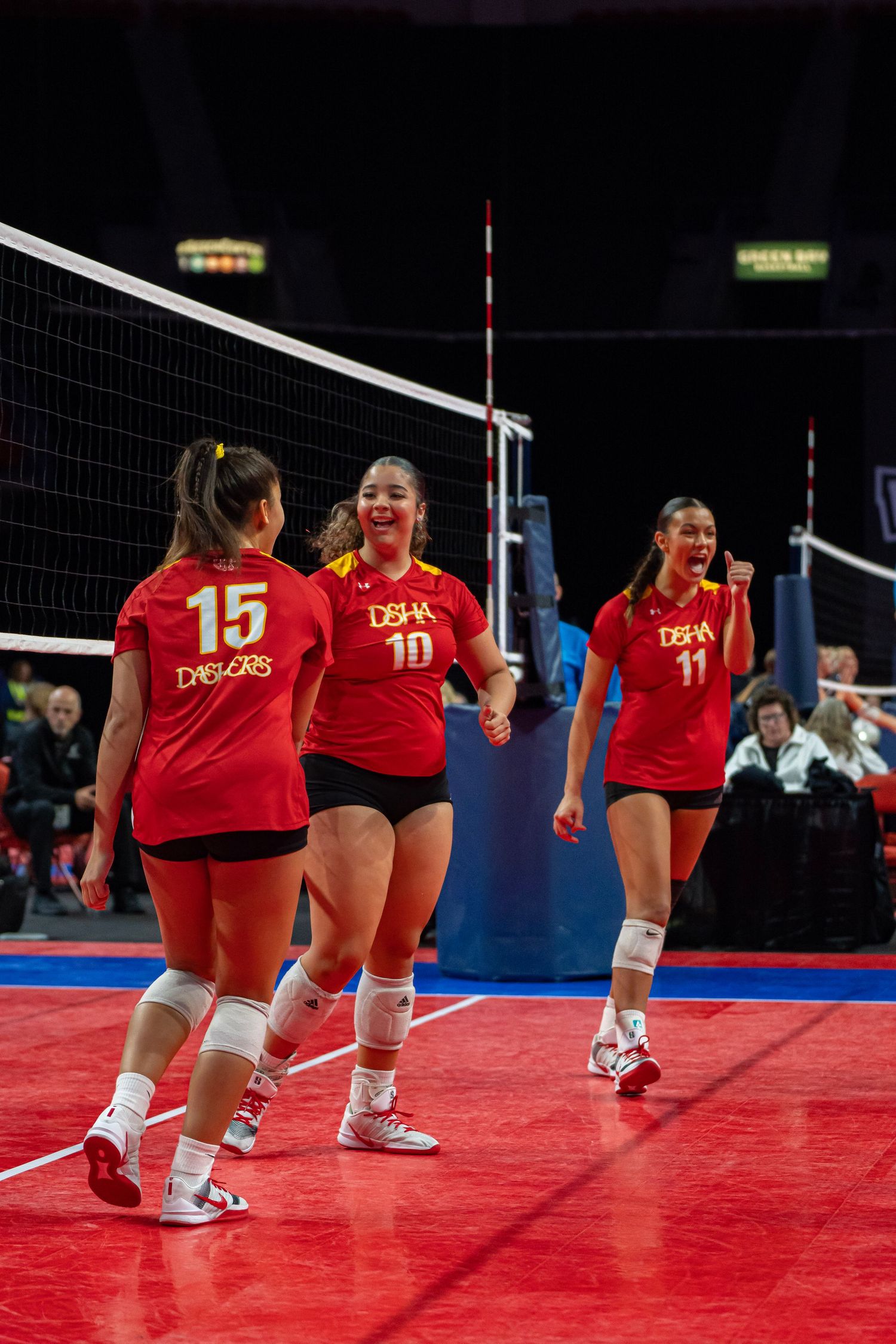 A sequence of volleyball players in red uniforms diving and sliding across a bright red court during a match.