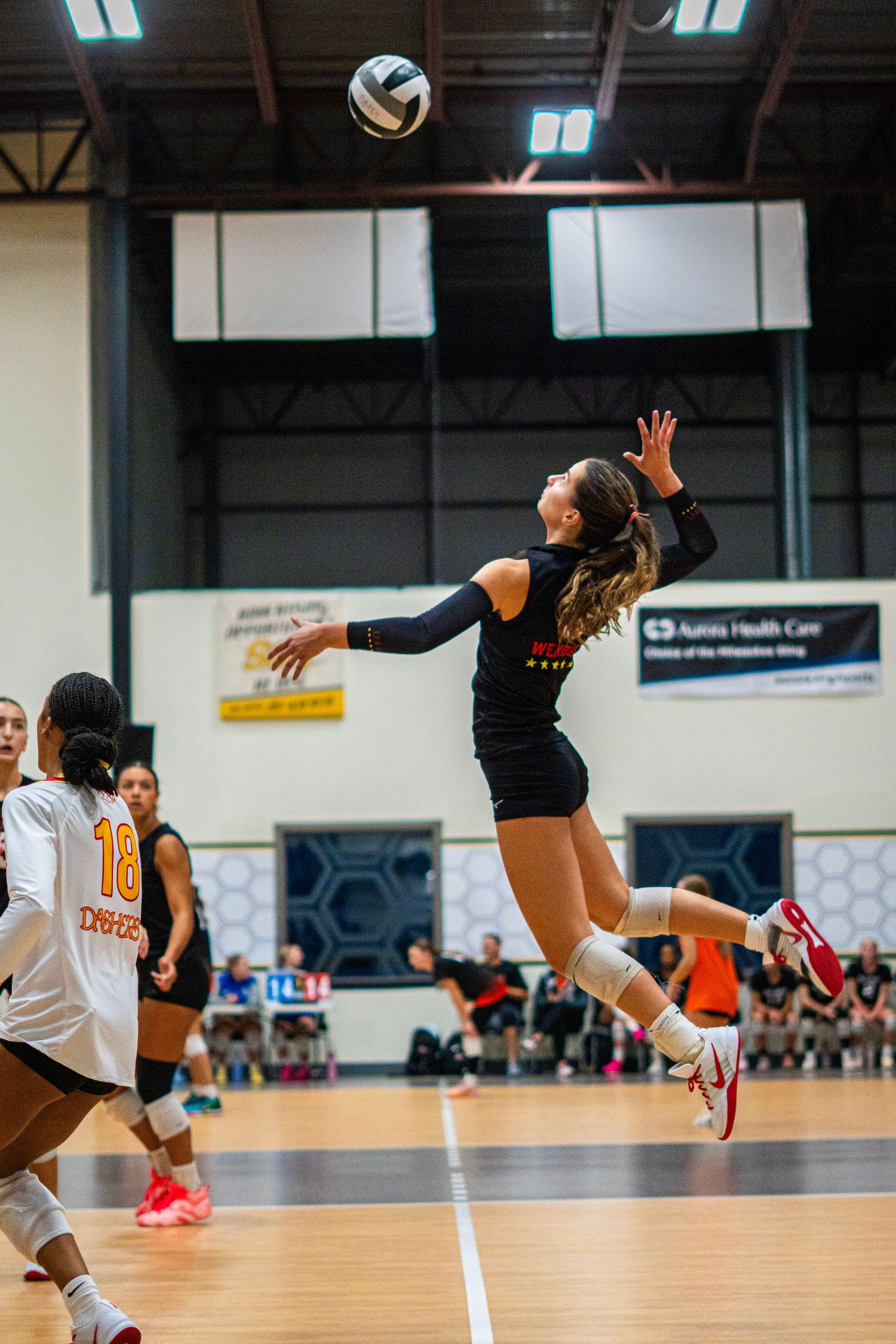 Athletic player leaps high to spike volleyball during competitive indoor match.