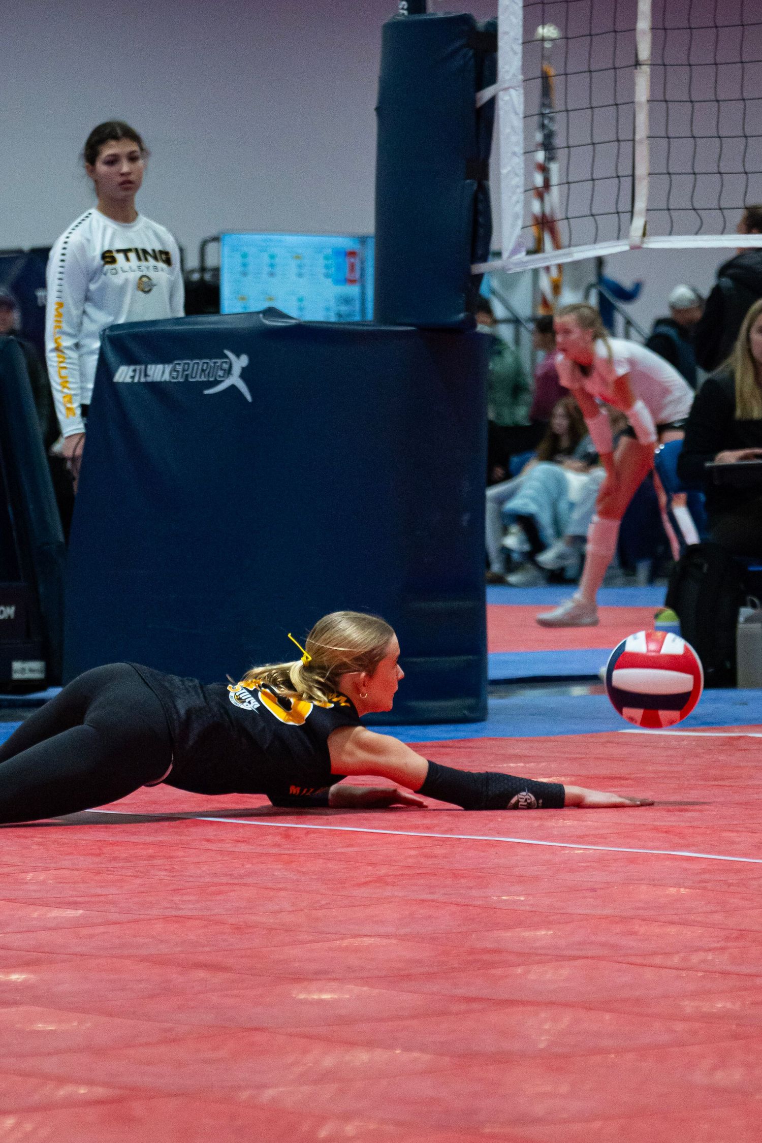 Female volleyball player diving on red court floor to save ball during indoor tournament match.