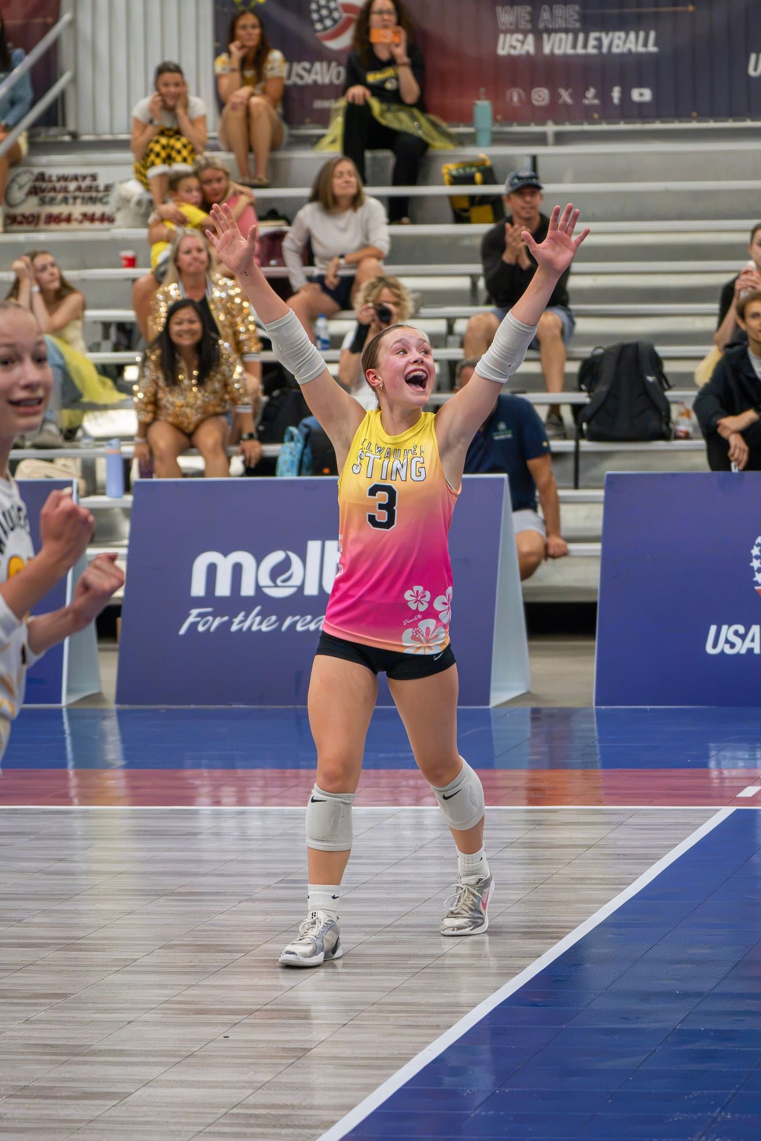 Female volleyball player #3 in pink jersey celebrates with arms raised at USA Volleyball indoor court tournament.