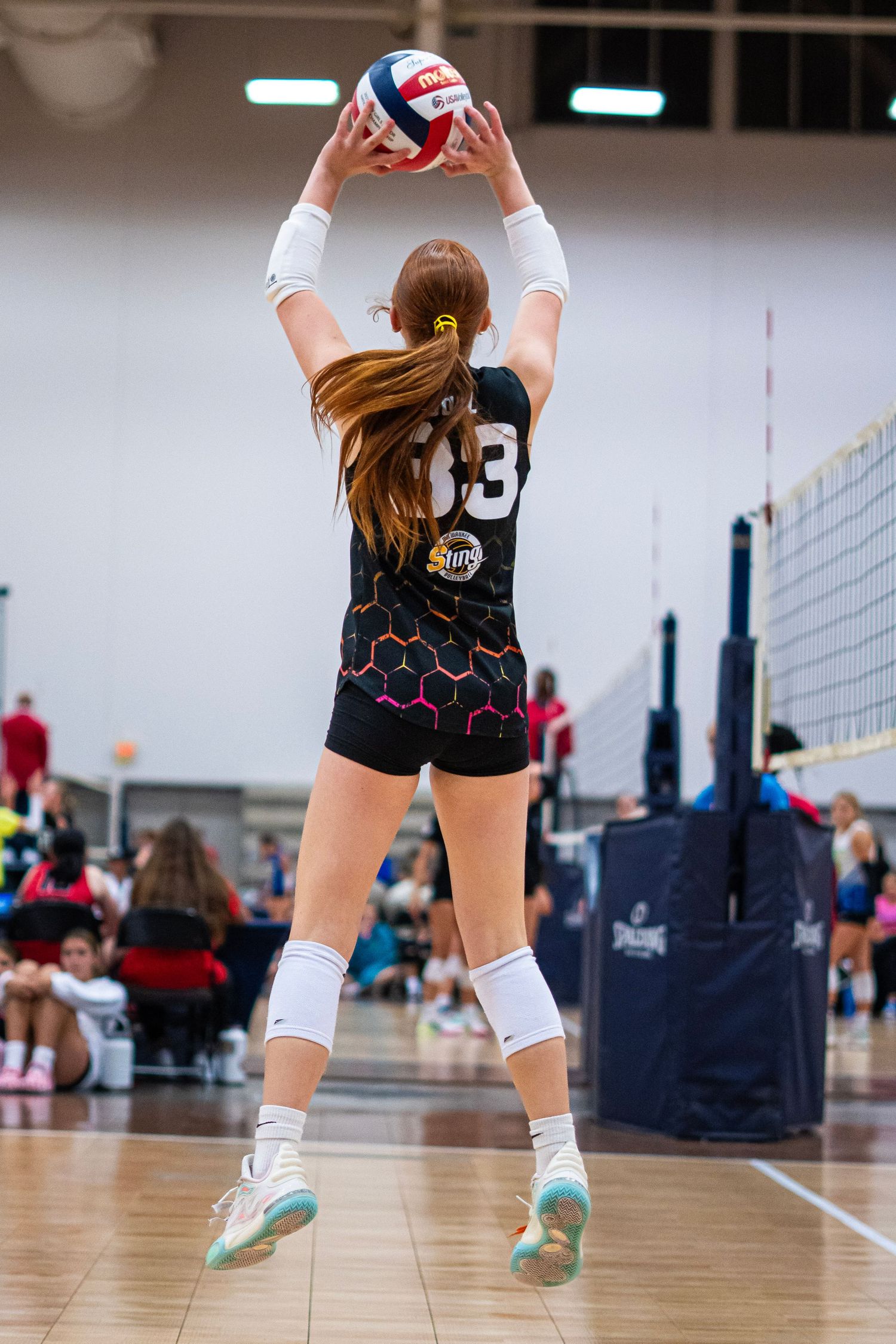 Volleyball players' legs and feet shown on indoor court wearing knee pads and athletic shoes.