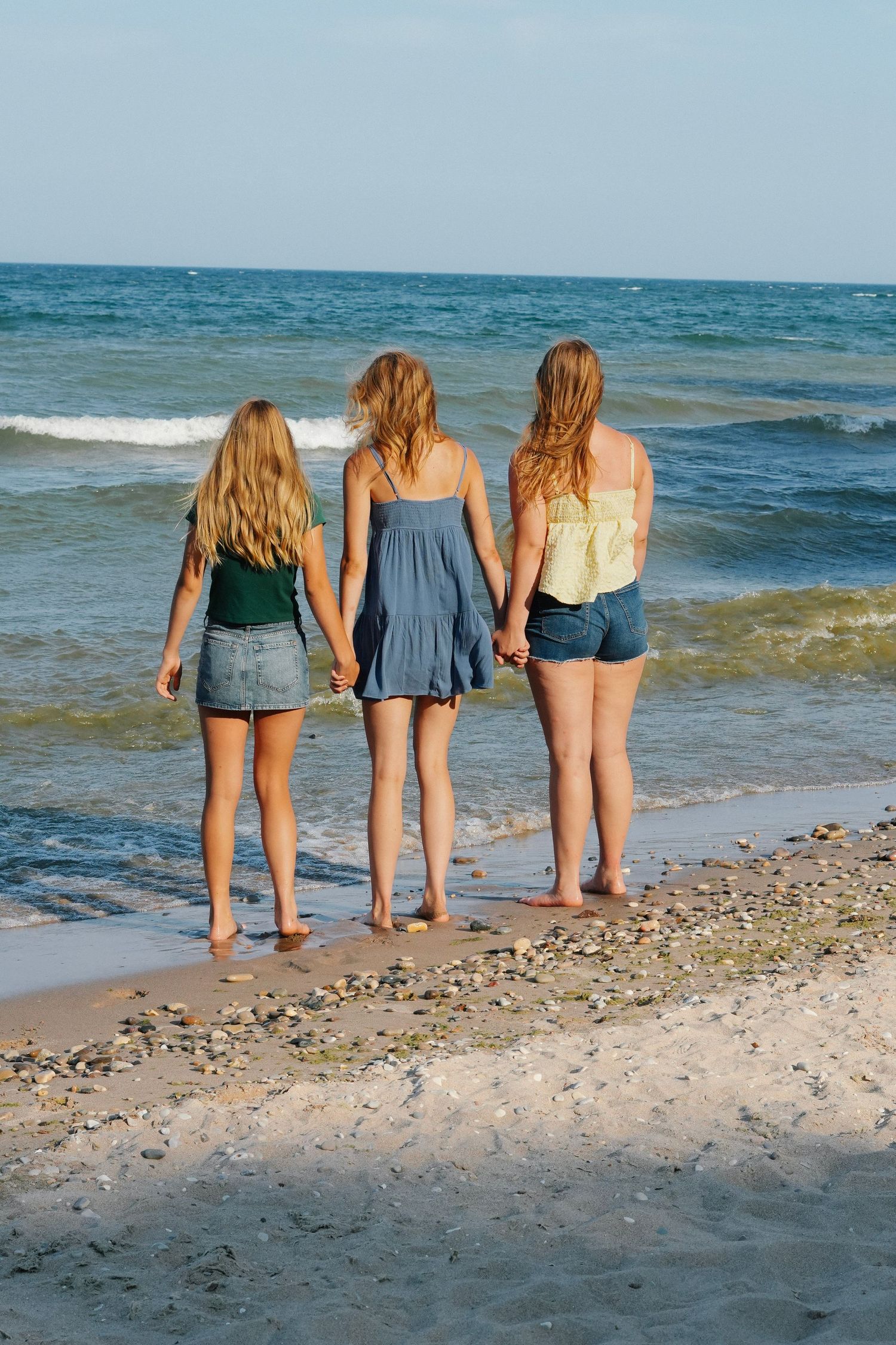 Group standing at beach edge looking out at blue ocean waves.