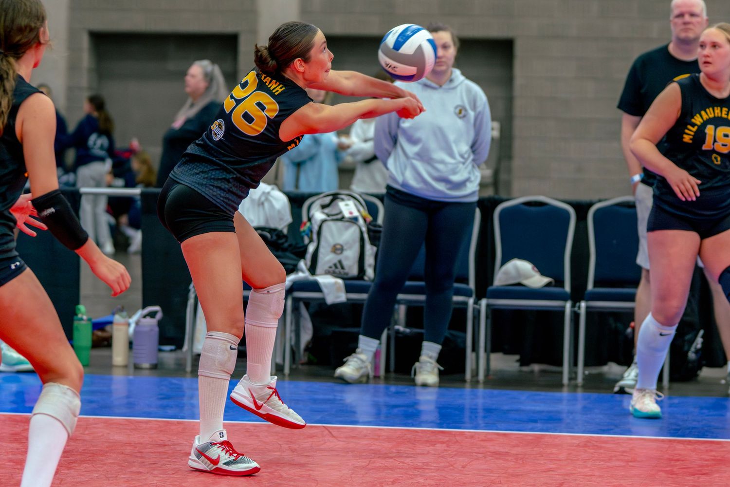 Female volleyball player in yellow jersey bumping ball during indoor tournament match.
