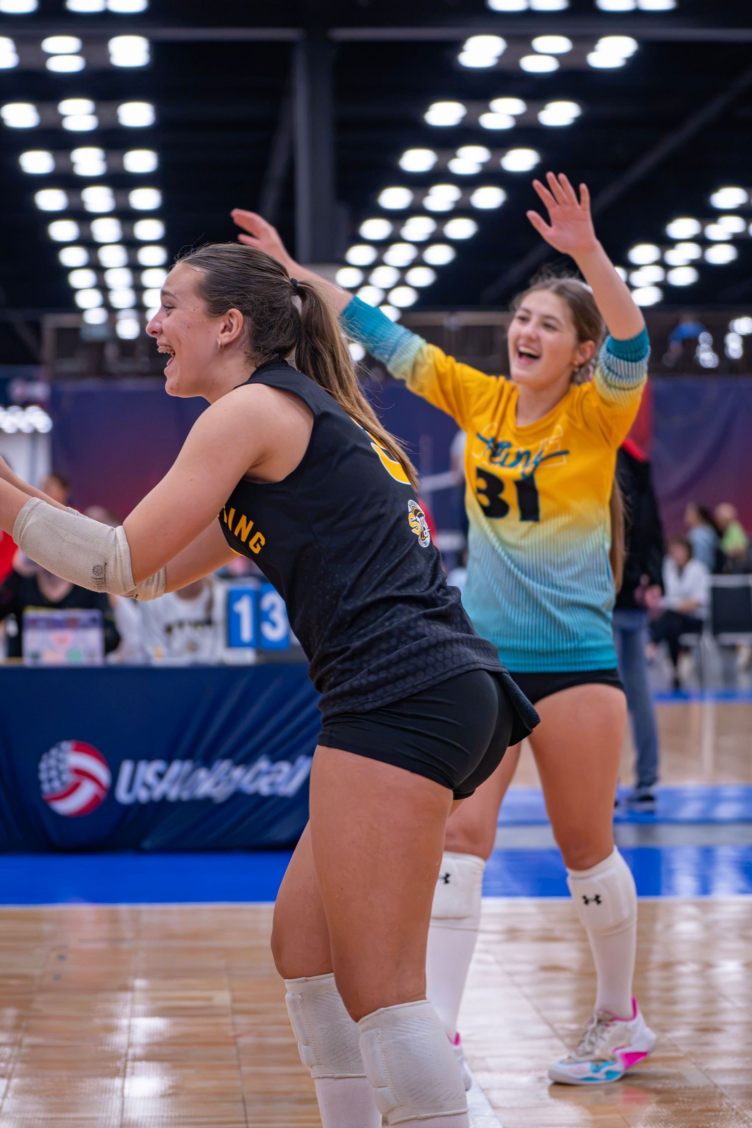 Two volleyball players celebrate a point during a USA Volleyball tournament match indoors.