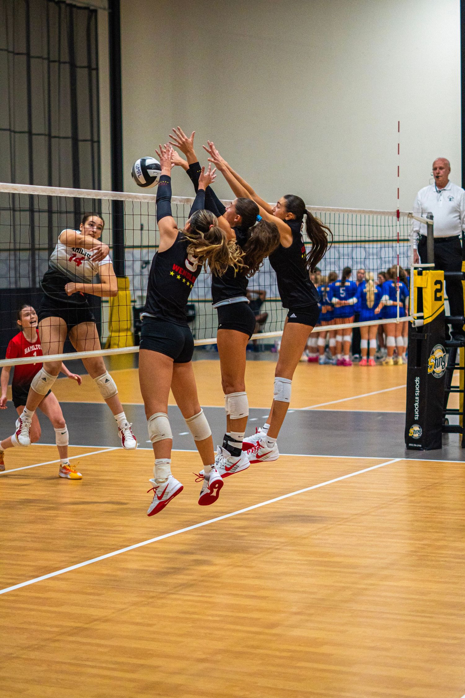 Team of volleyball players jumping in unison to block at the net.