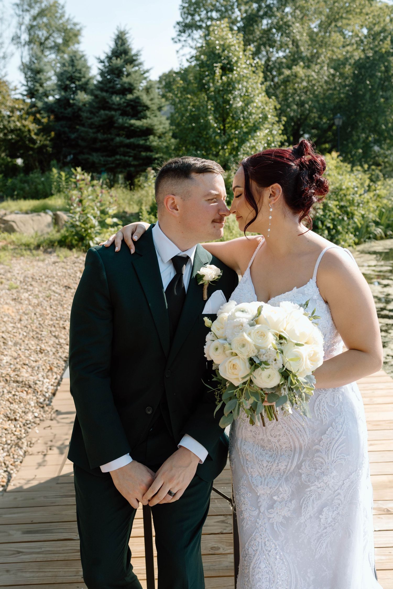 Wedding couple shares intimate kisses outdoors with white roses against a natural backdrop.