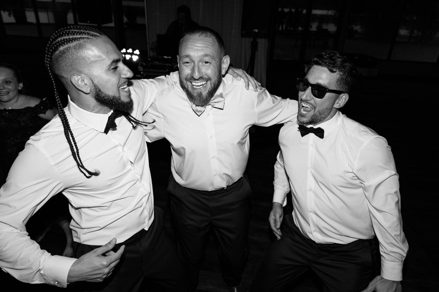 Wedding party members in formal attire share candid laughs during black and white reception photos.