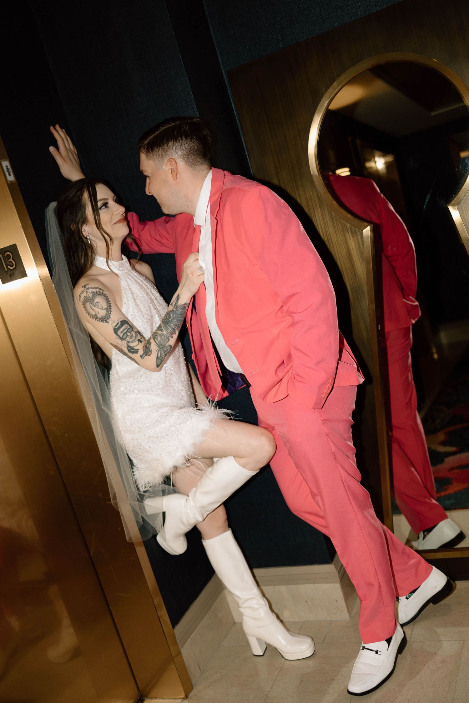Wedding couple in white dress and red attire sharing playful moments in a dimly lit venue.
